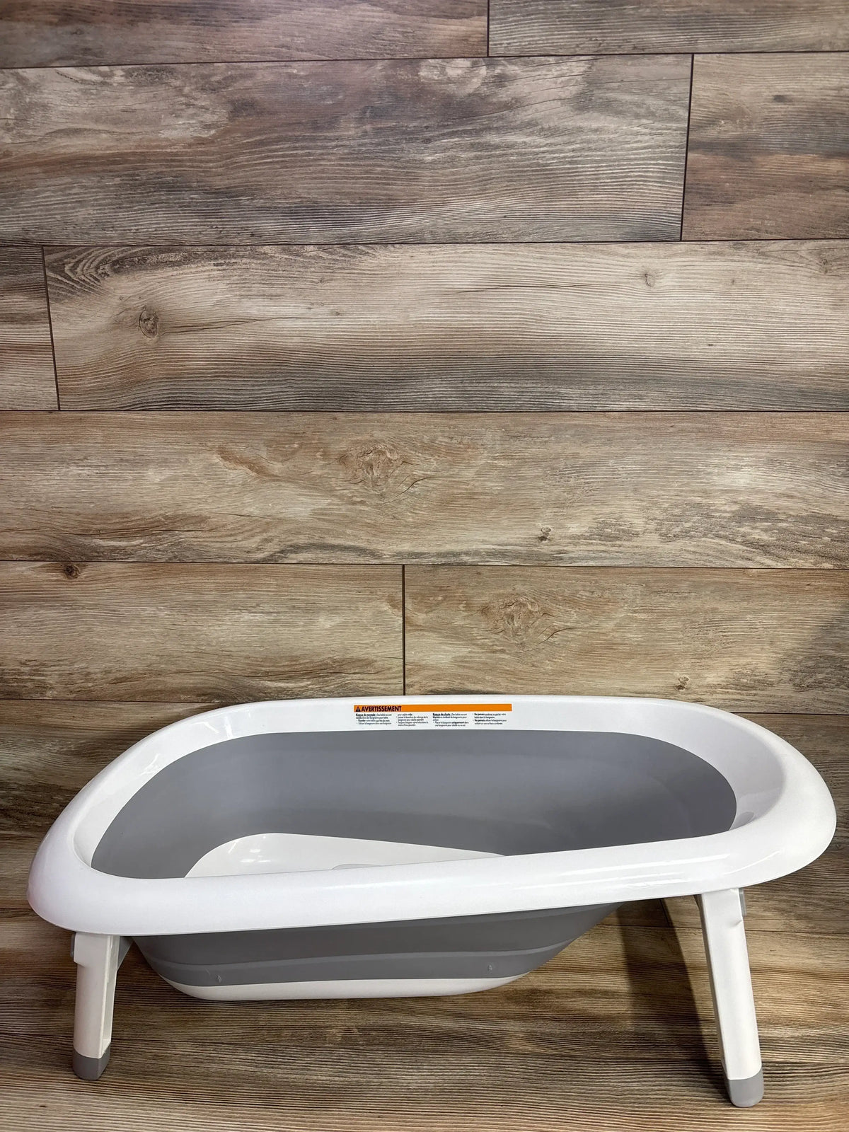 Angled side view of OXO Tot Splash & Store Bathtub Grey showcasing fold-out legs and collapsible design on wood floor