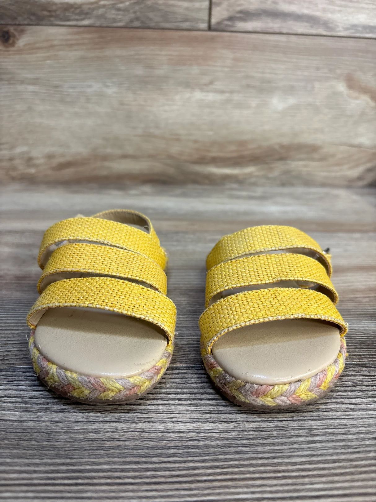Yellow woven kids sandals with braided soles on wood background