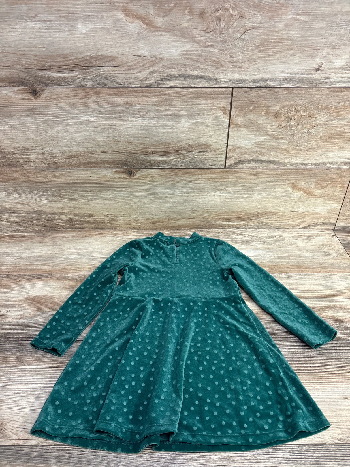 Teal long sleeve velvet polka dot girl’s dress laid flat on wood background.