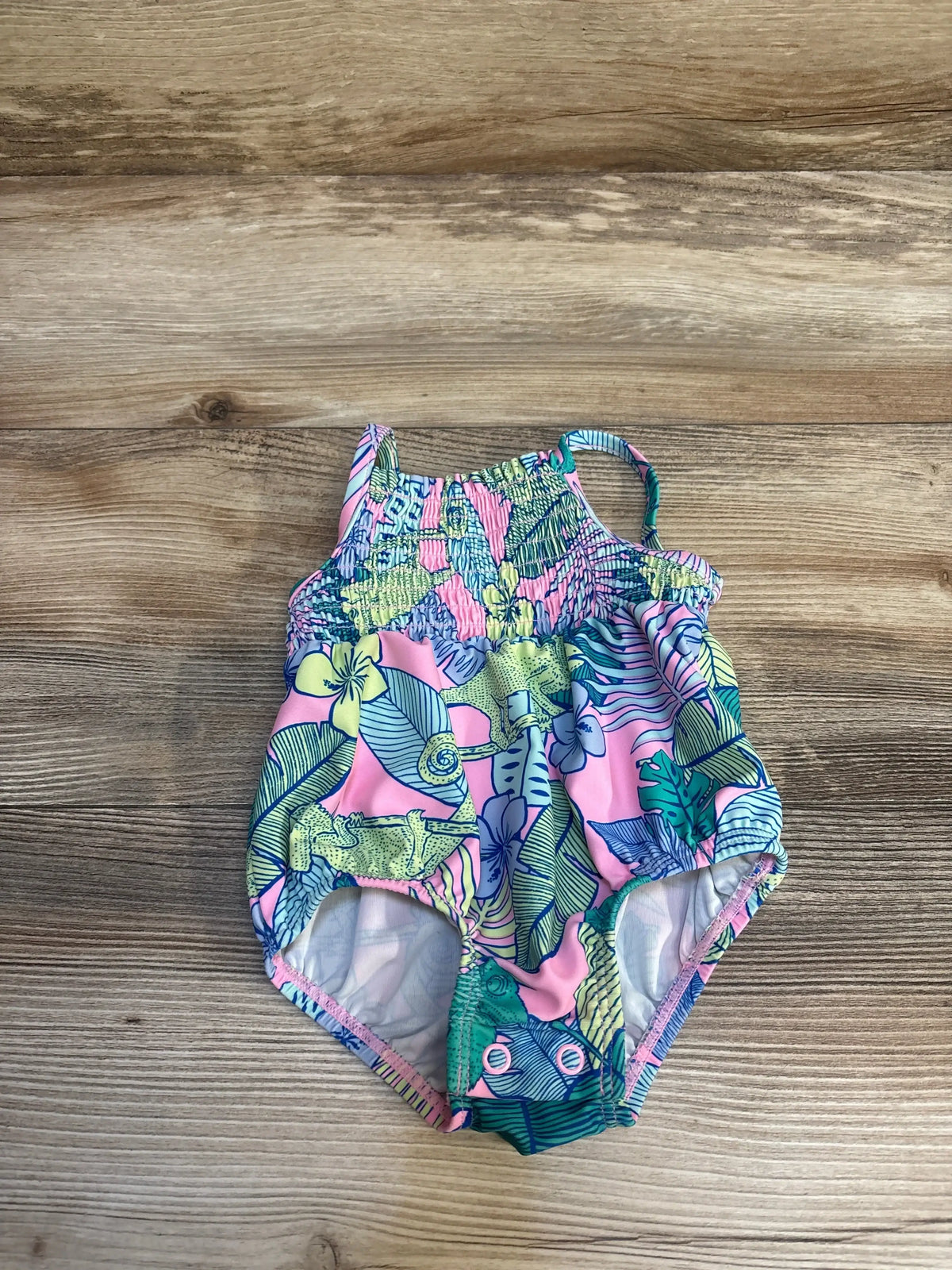 Colorful floral baby swimsuit with pink, green, and blue tropical pattern on wood background