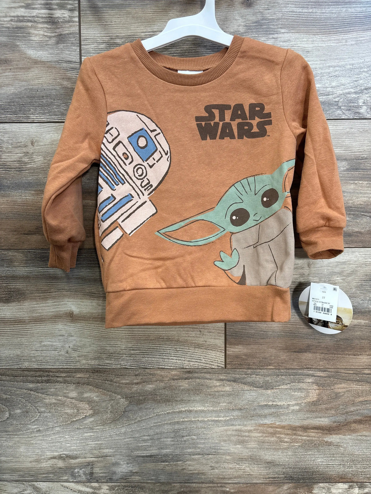 Front view of a caramel Star Wars sweatshirt in size 2T showcasing R2-D2 and Grogu graphics on a hanger against a wood-grain background