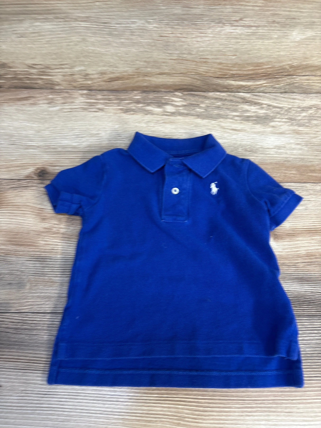 Royal blue kids polo shirt with white logo, short sleeves, laid on wood floor