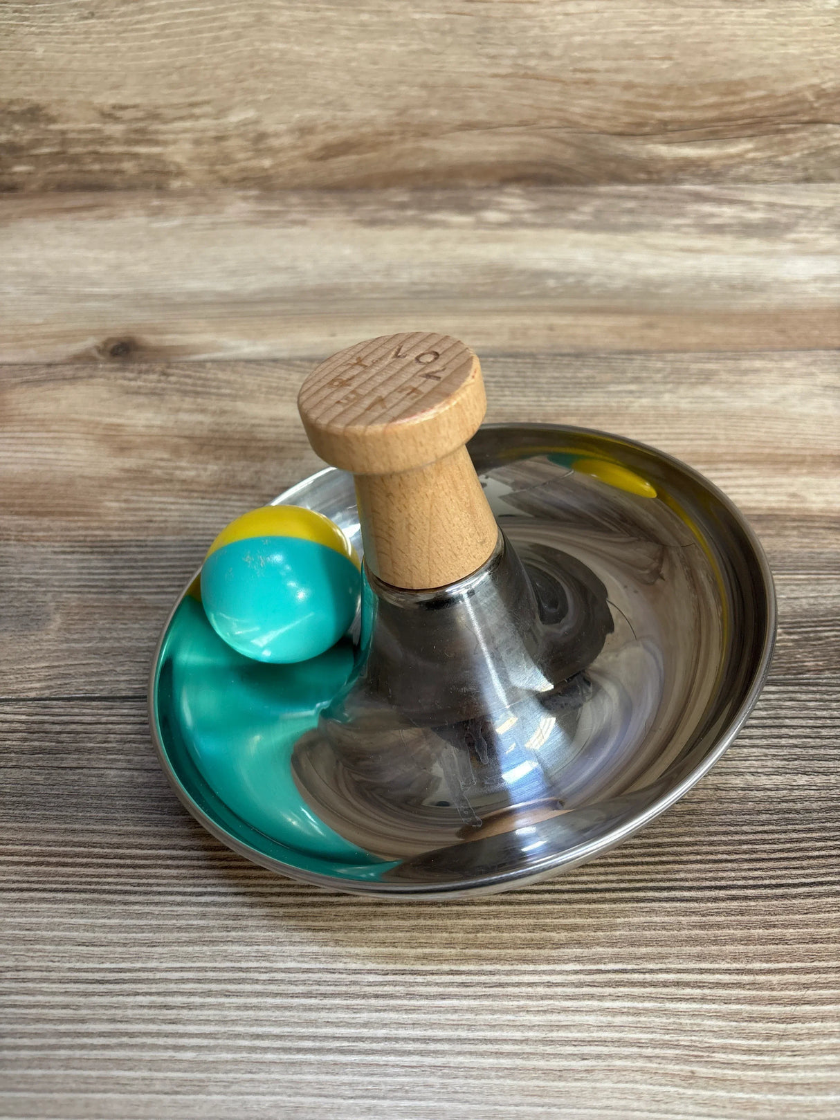 Stainless steel Indian spice masher with wooden handle and blue ball on wood surface
