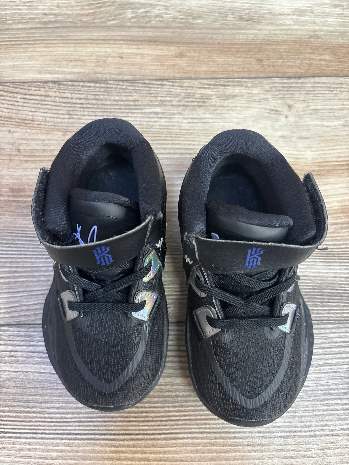 Pair of black toddler basketball shoes with Kyrie Irving logo on wooden floor