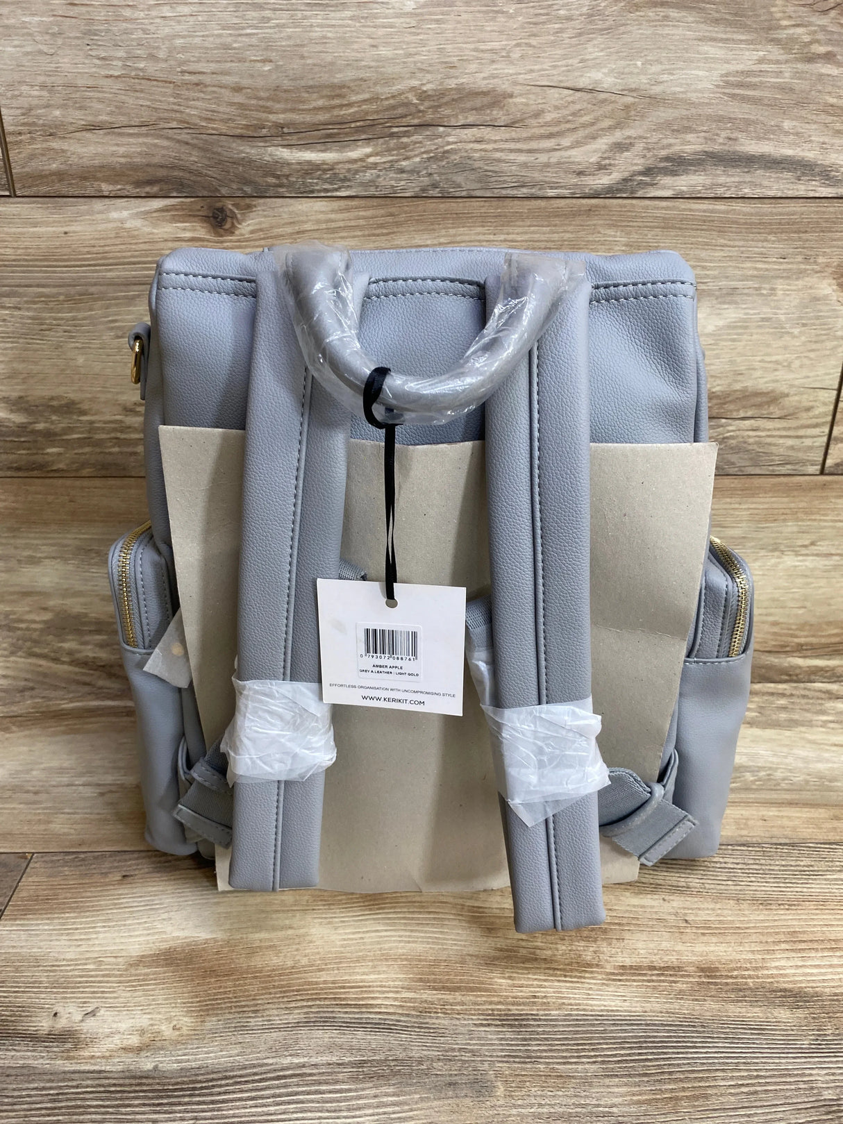 Light gray backpack diaper bag with padded straps and gold zippers on wood background