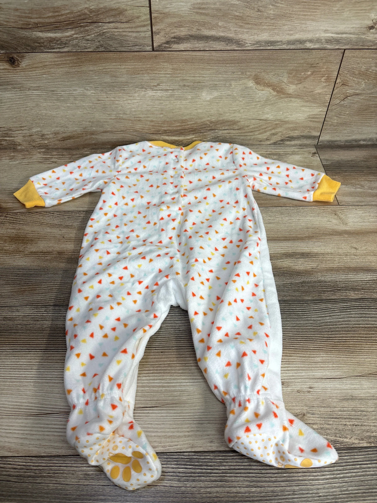 White baby sleeper with colorful triangle print and yellow cuffs, laid flat on wood floor