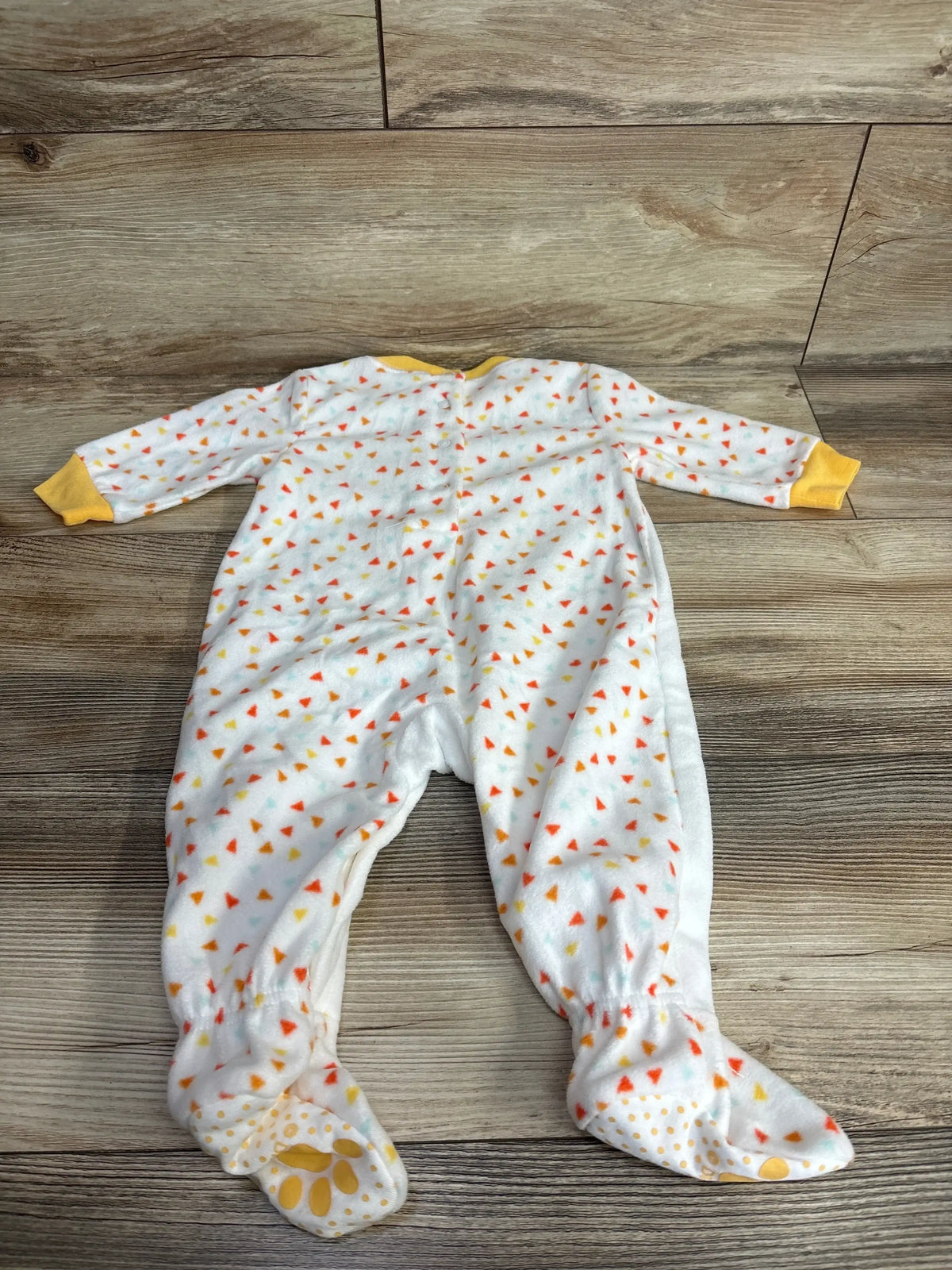 White baby sleeper with colorful triangle print and yellow cuffs, laid flat on wood floor