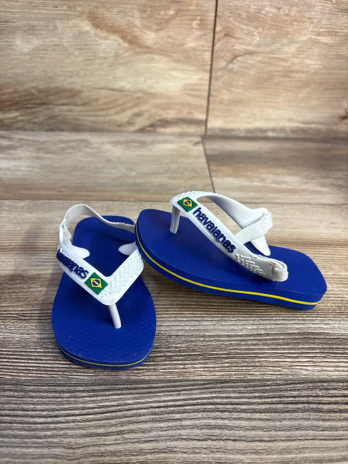 Front and side view of Havaianas blue flip flops, size 6C, showcasing white elastic ankle straps on a wood-grain surface