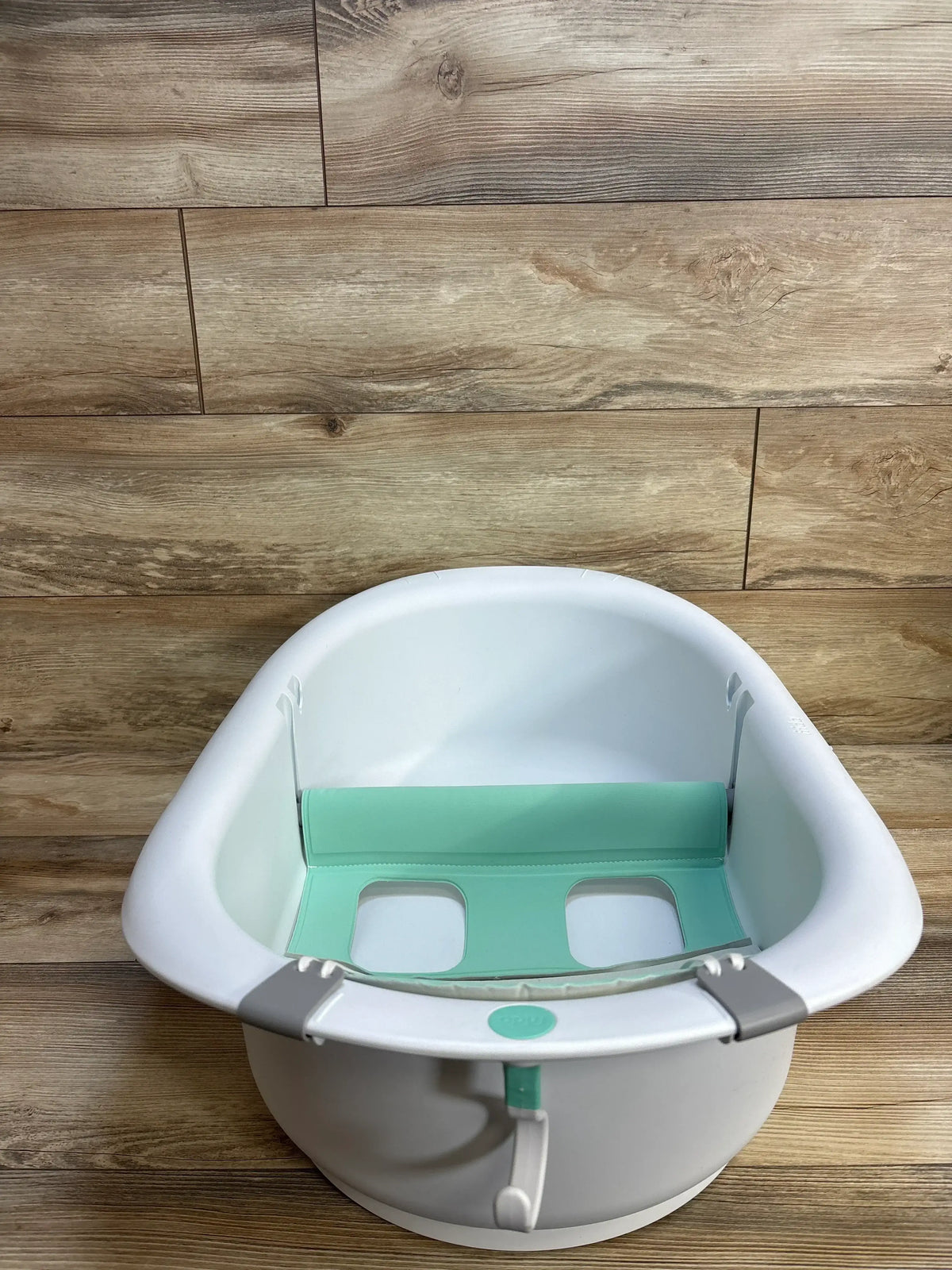 Front view of Frida Baby 4-in-1 Grow-With-Me Bath Tub with mint infant support insert, leg openings, and gray clips