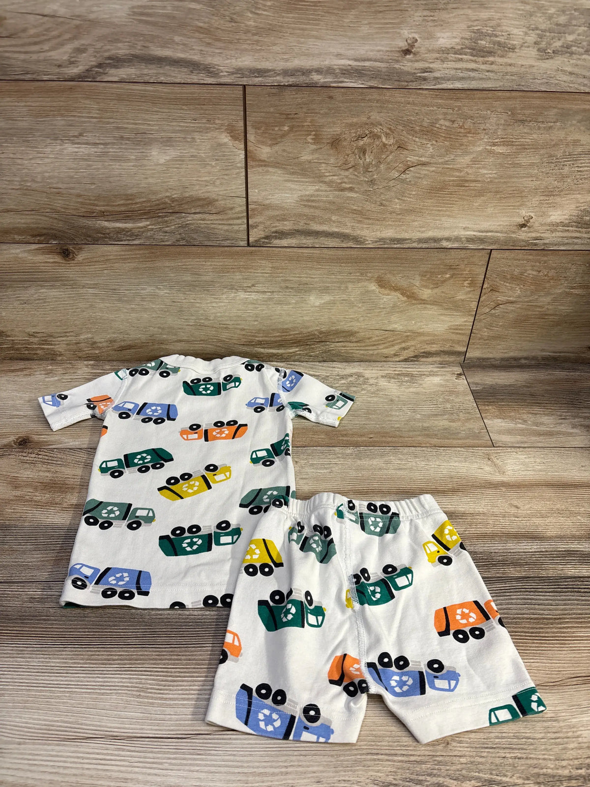 Flat lay of Hanna Andersson 2-piece ivory short johns pajama set showing colorful recycled truck print on wood background