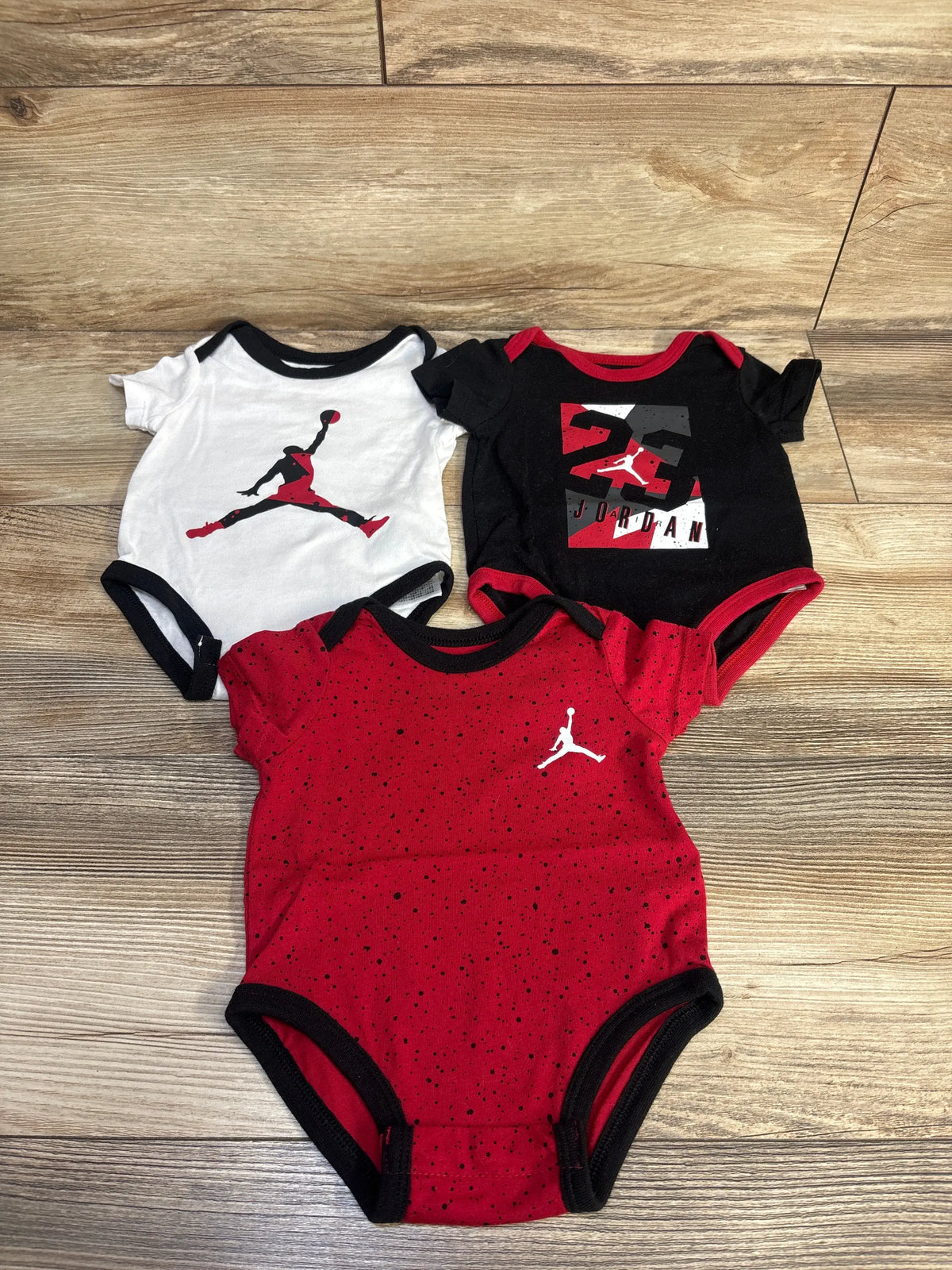Top view of Jordan 3-pack bodysuits showcasing short sleeves and contrasting trim with a wood-look floor