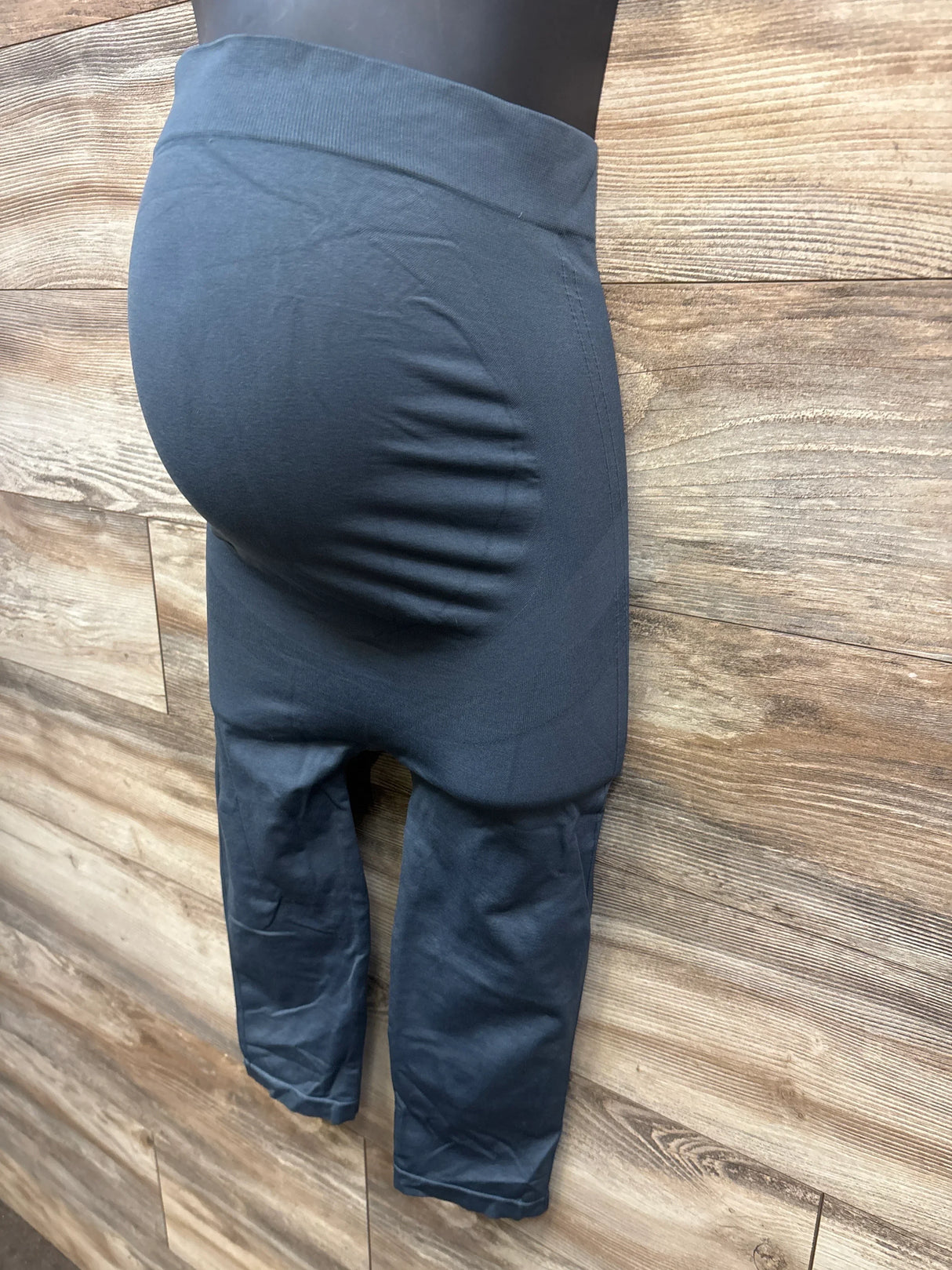 Side view of grey Blanqi belly support capri maternity leggings showcasing high-rise belly panel against wood background
