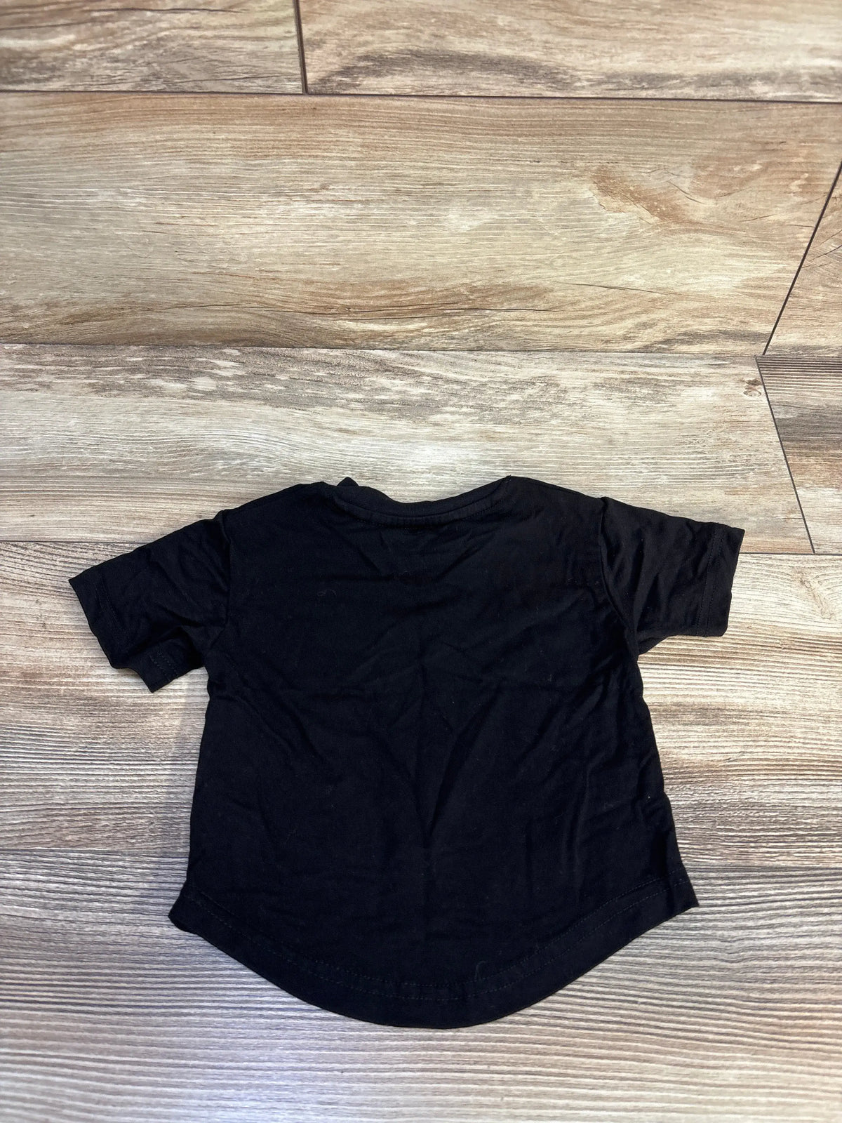 Front view of Little Bipsy black bamboo shirt in size 3 to 6 months showcasing short sleeves and curved hem on a wood floor
