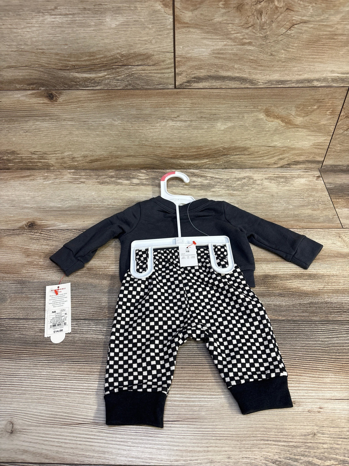 Flat lay of newborn 2-piece sweatshirt and joggers showing charcoal top and black-and-white checkered pants on wood background