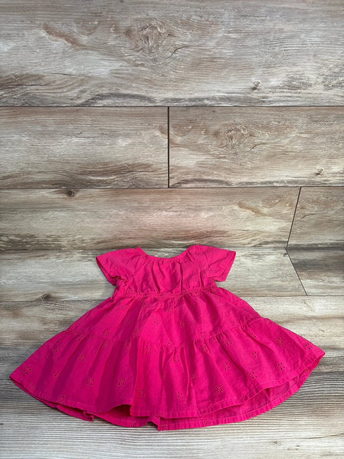 Pink short sleeve toddler dress with eyelet pattern on wood background