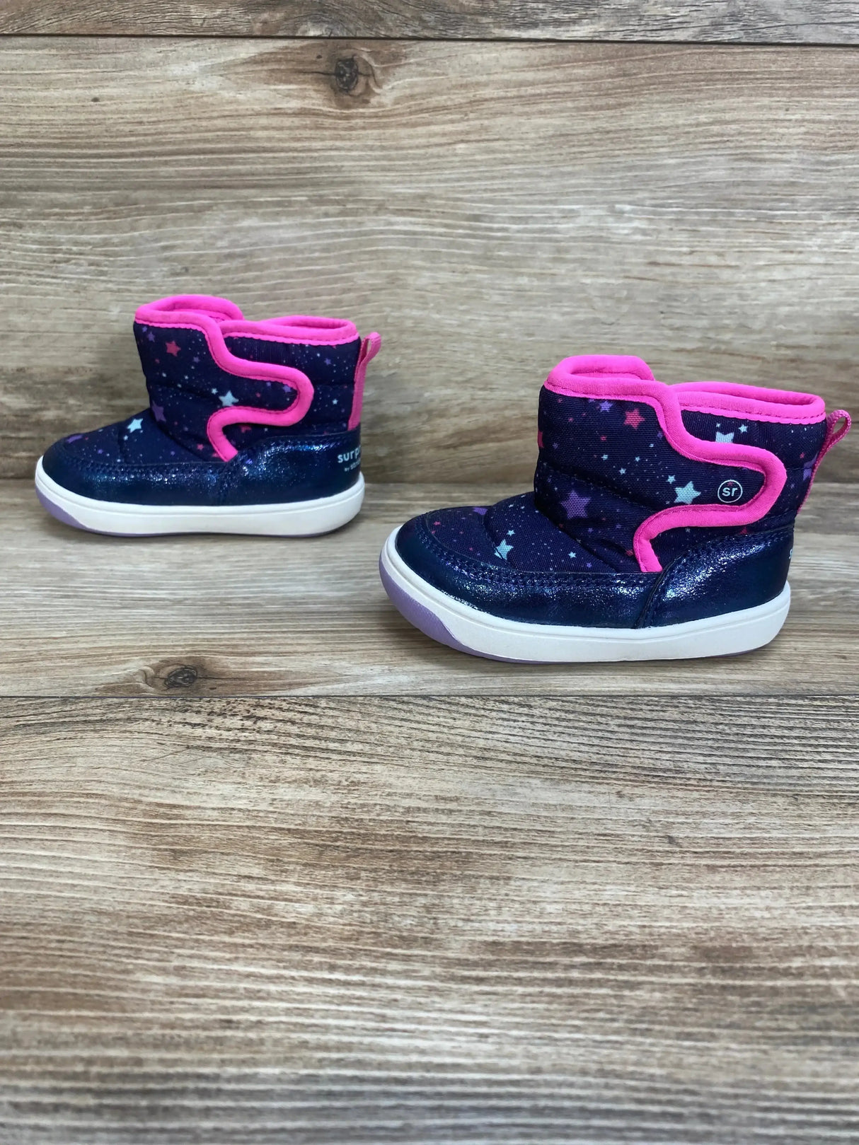 Right-front view of Surprize by Stride Rite Aster winter boot size 4C showcasing navy star print, pink trim, hook-and-loop closure and white sole on wood background