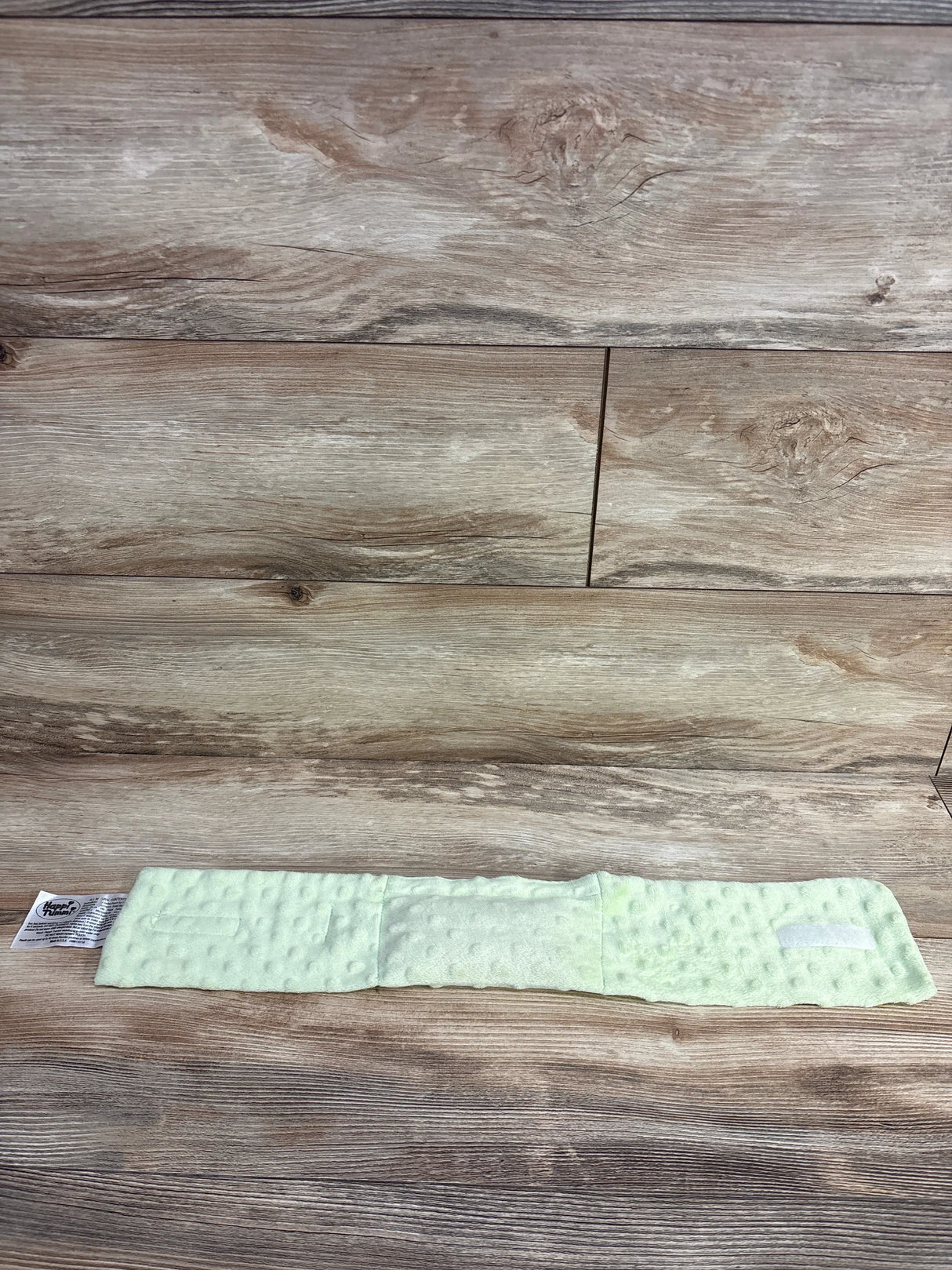 Flat lay of Happi Tummi colic relief waistband in light green minky with Velcro and dimpled texture on wood background