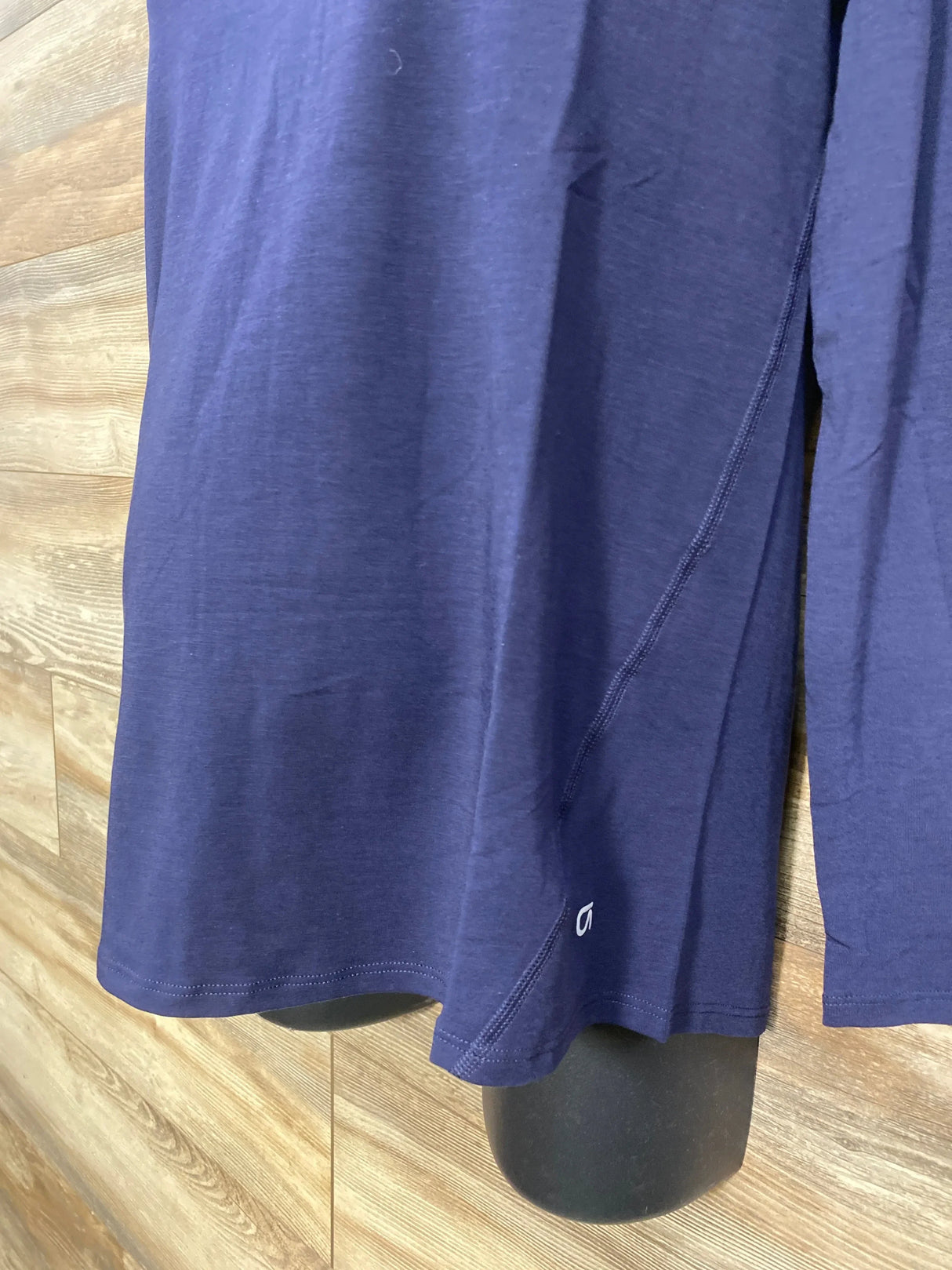 Front lower view of Gap maternity navy long-sleeve shirt showing side seam, hem, and small white logo on wood-paneled background