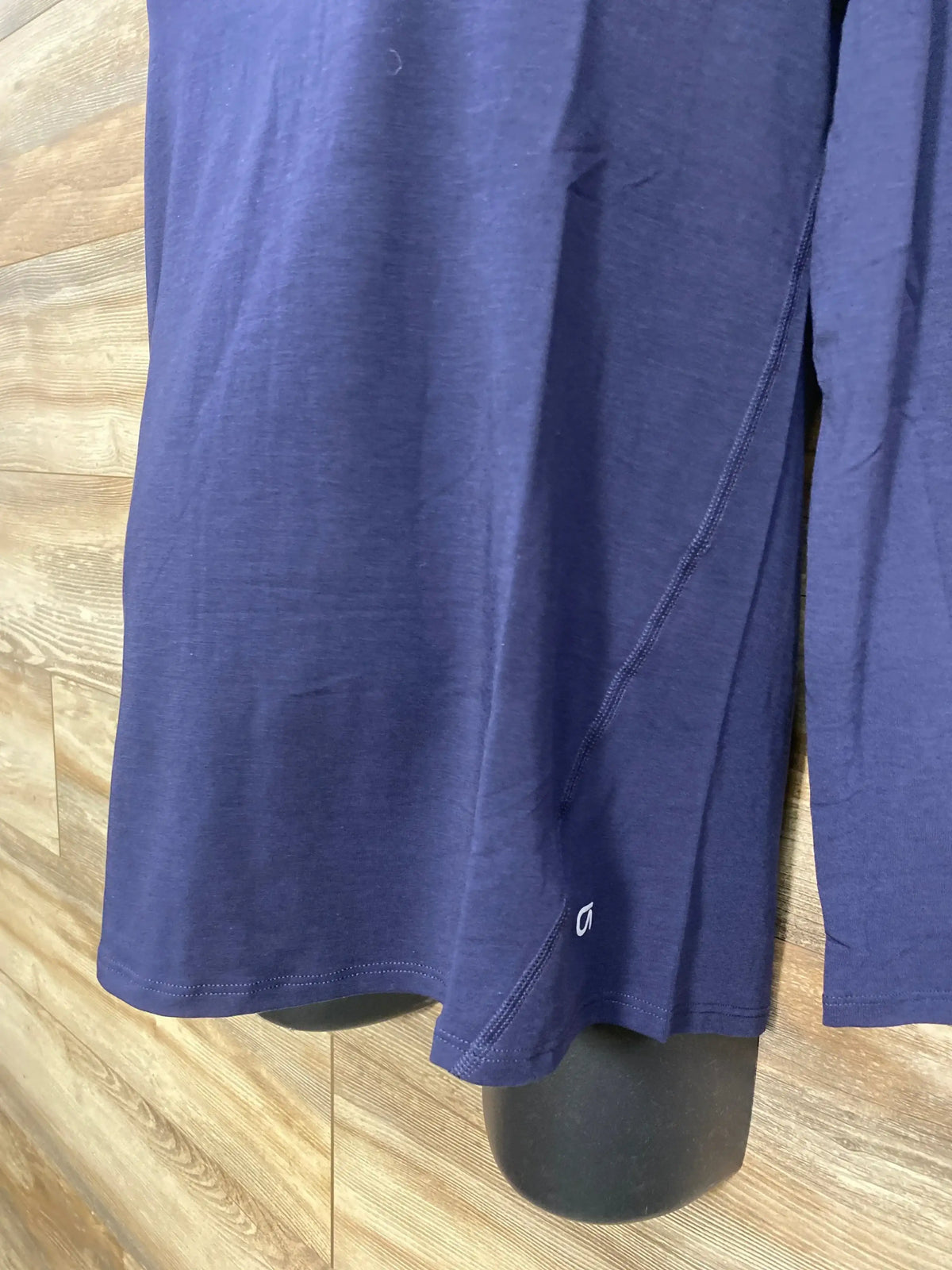 Front lower view of Gap maternity navy long-sleeve shirt showing side seam, hem, and small white logo on wood-paneled background