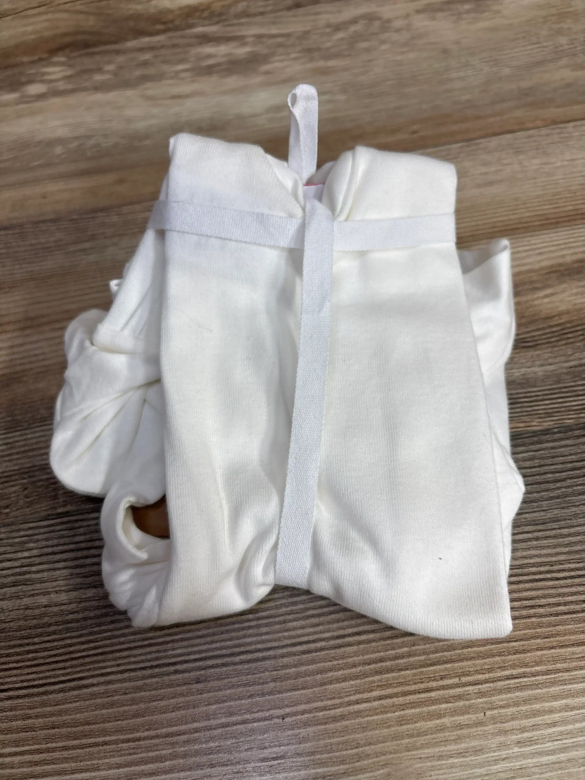 White baby onesie with snap closure, folded on wood floor, soft cotton infant clothing