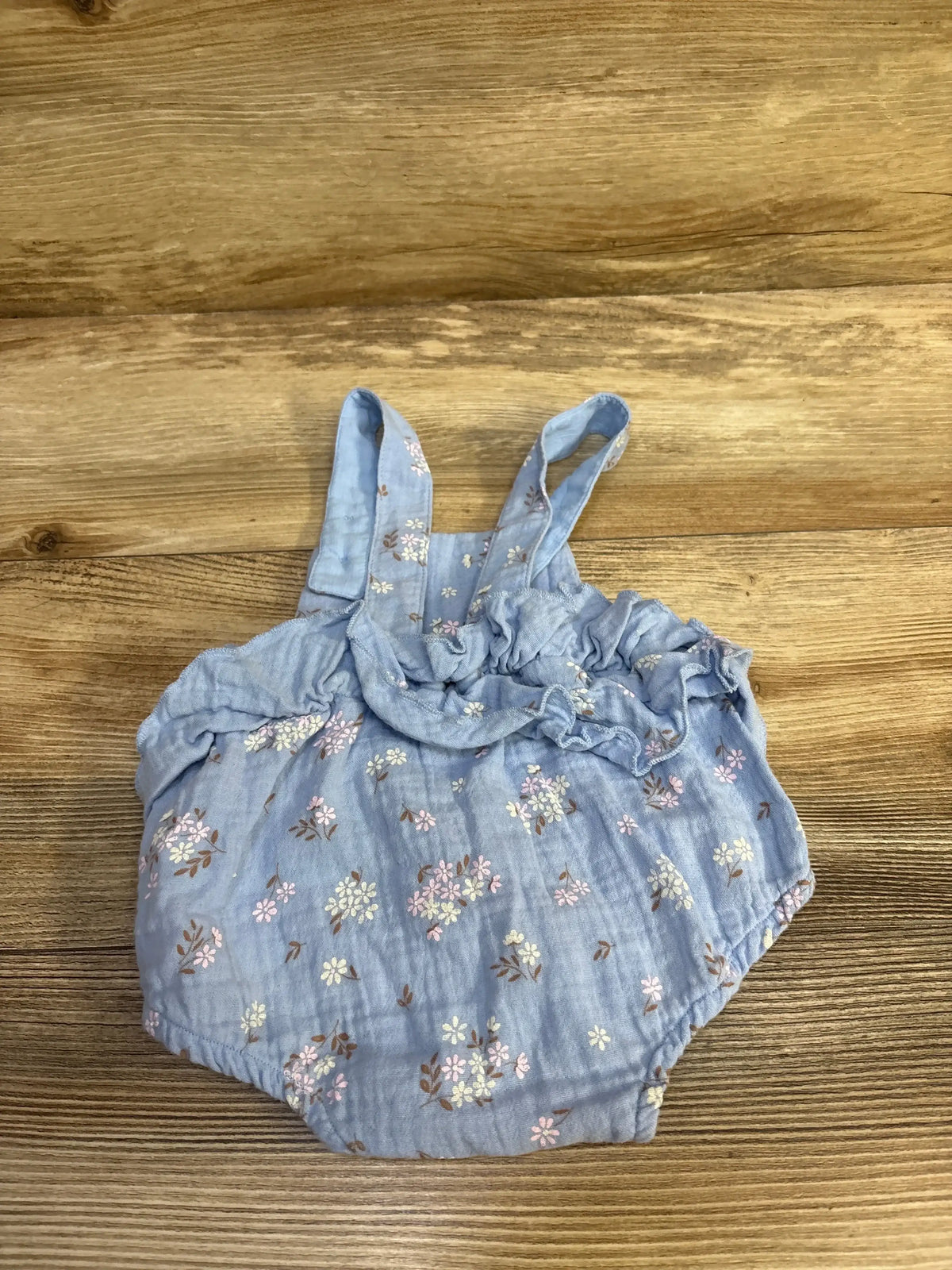 Flat lay of Purebaby floral ruffle bubble romper in blue with floral print and ruffled shoulders on wood plank floor