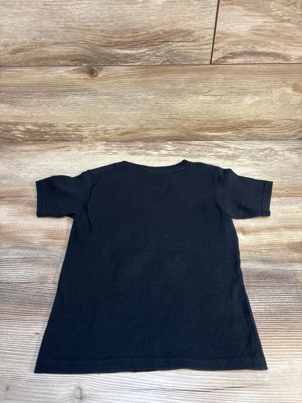 Black short sleeve kids t-shirt laid flat on wooden floor