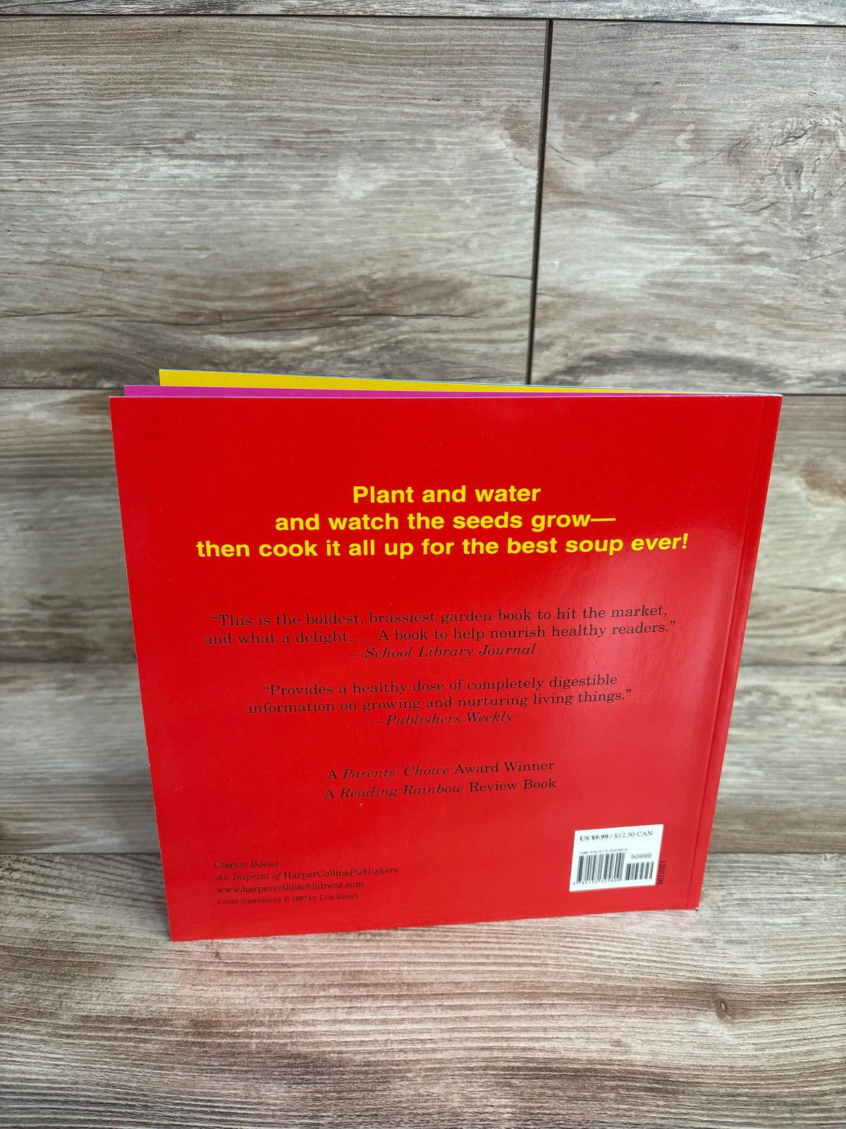 Back cover of a red gardening book with yellow text about planting seeds and cooking soup, on wooden surface
