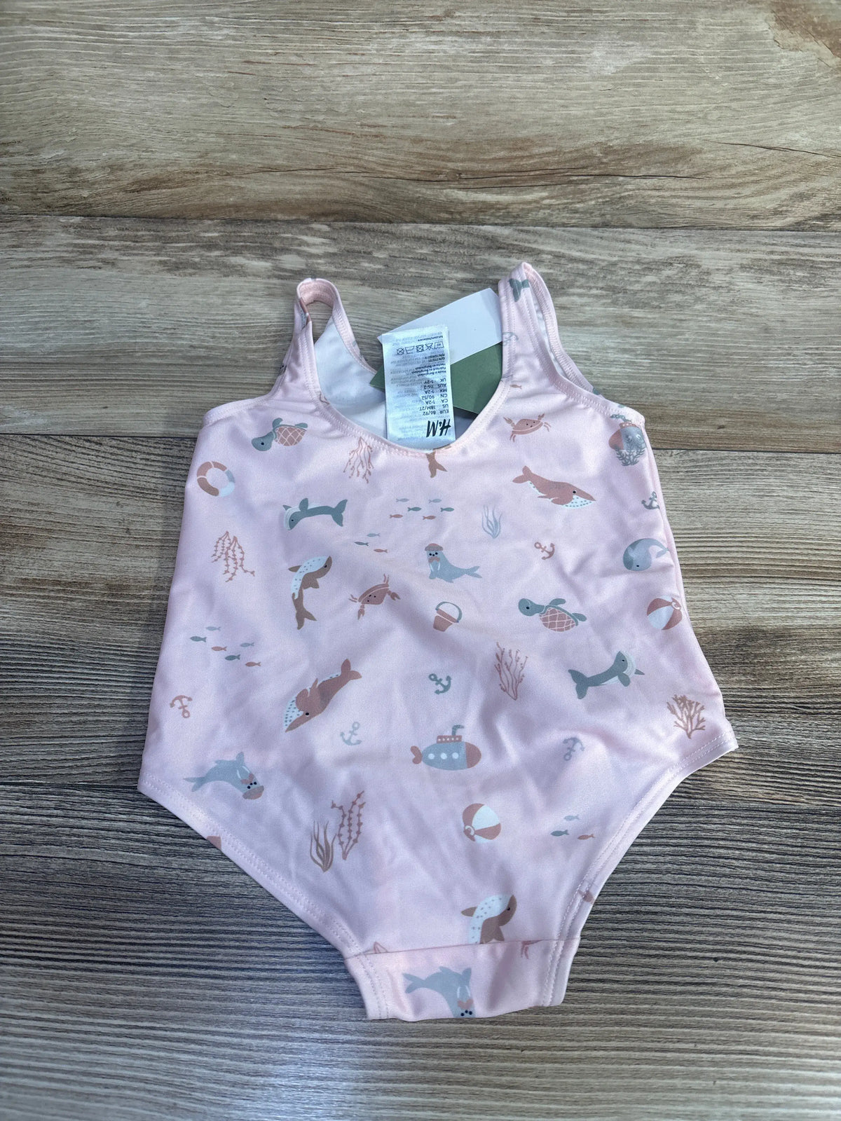 Front view of H&M pink patterned one-piece swimsuit showcasing aquatic print and shoulder straps on a wood surface