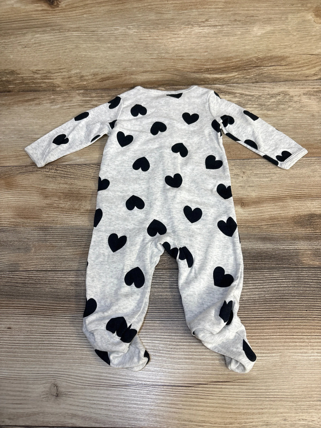 Gray baby sleeper with black heart print, long sleeves, footed, on wood background