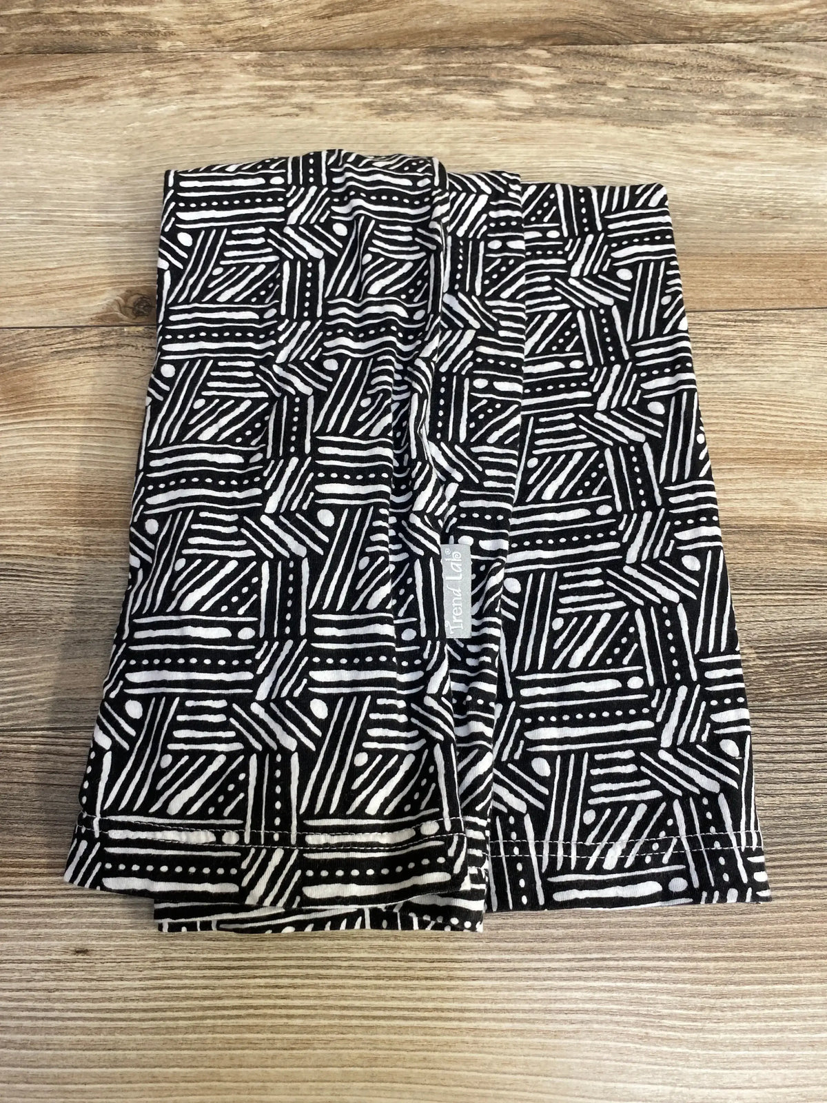 Flat lay of Trend Lab Geometric multi-use nursing cover showing black-and-white geometric print and brand tag on wood
