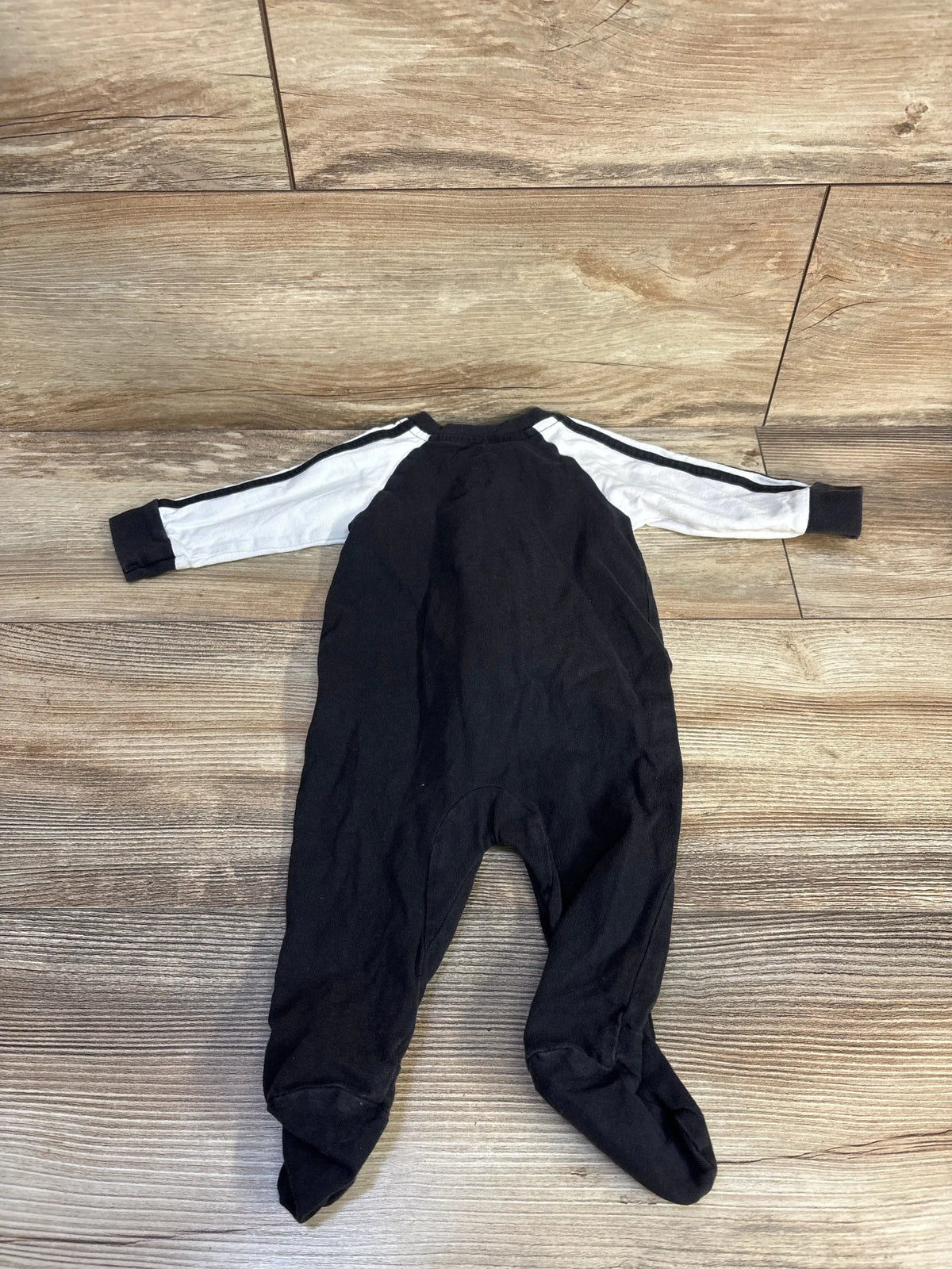 Front view of Adidas baby sleeper showcasing black footed legs and white striped sleeves on a wood-grain floor