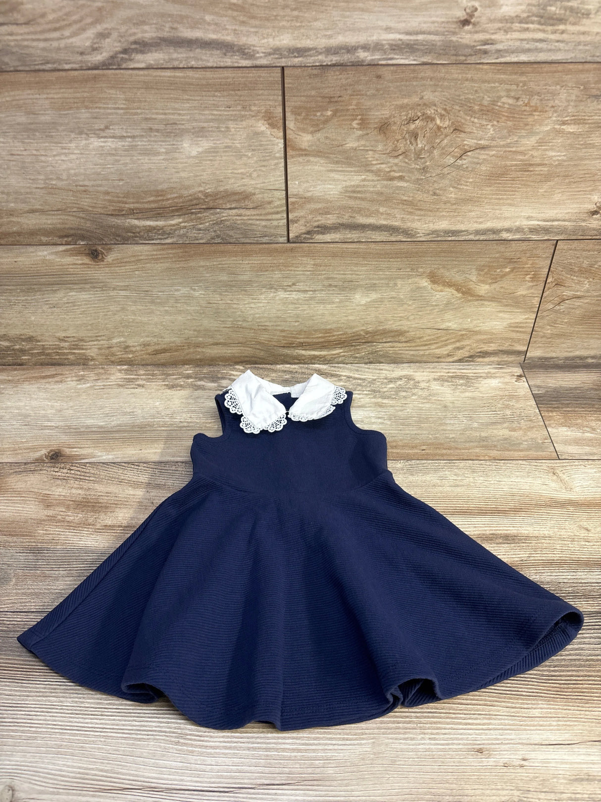 Flat lay of Janie and Jack sleeveless navy dress with white lace collar on wood background