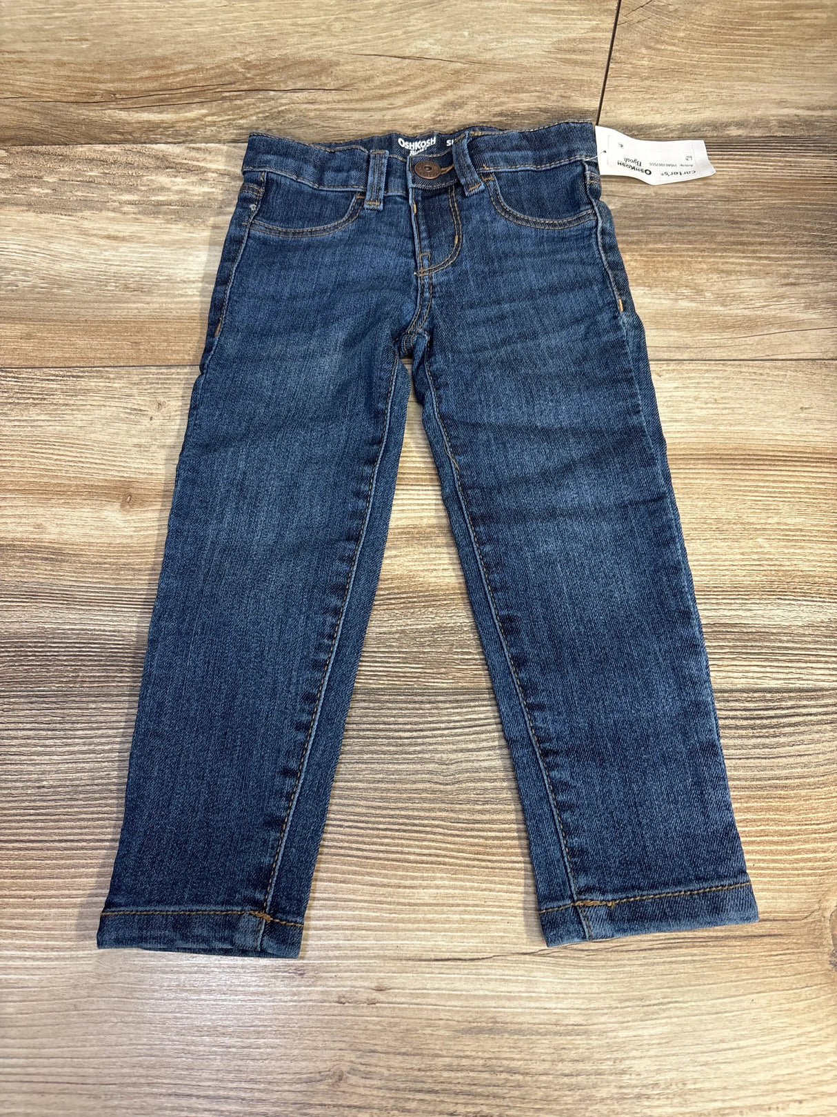 OshKosh blue denim jeans for kids displayed flat on wooden surface
