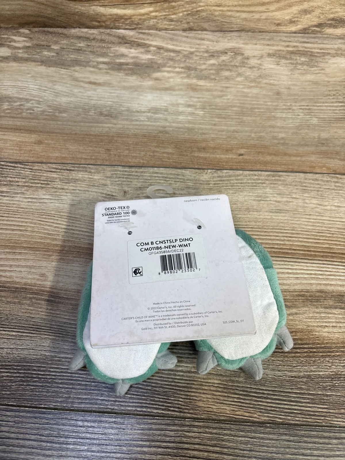 Underside view of Child Of Mine plush dinosaur claw slippers showcasing green plush trim and gray claws on a wood-look floor