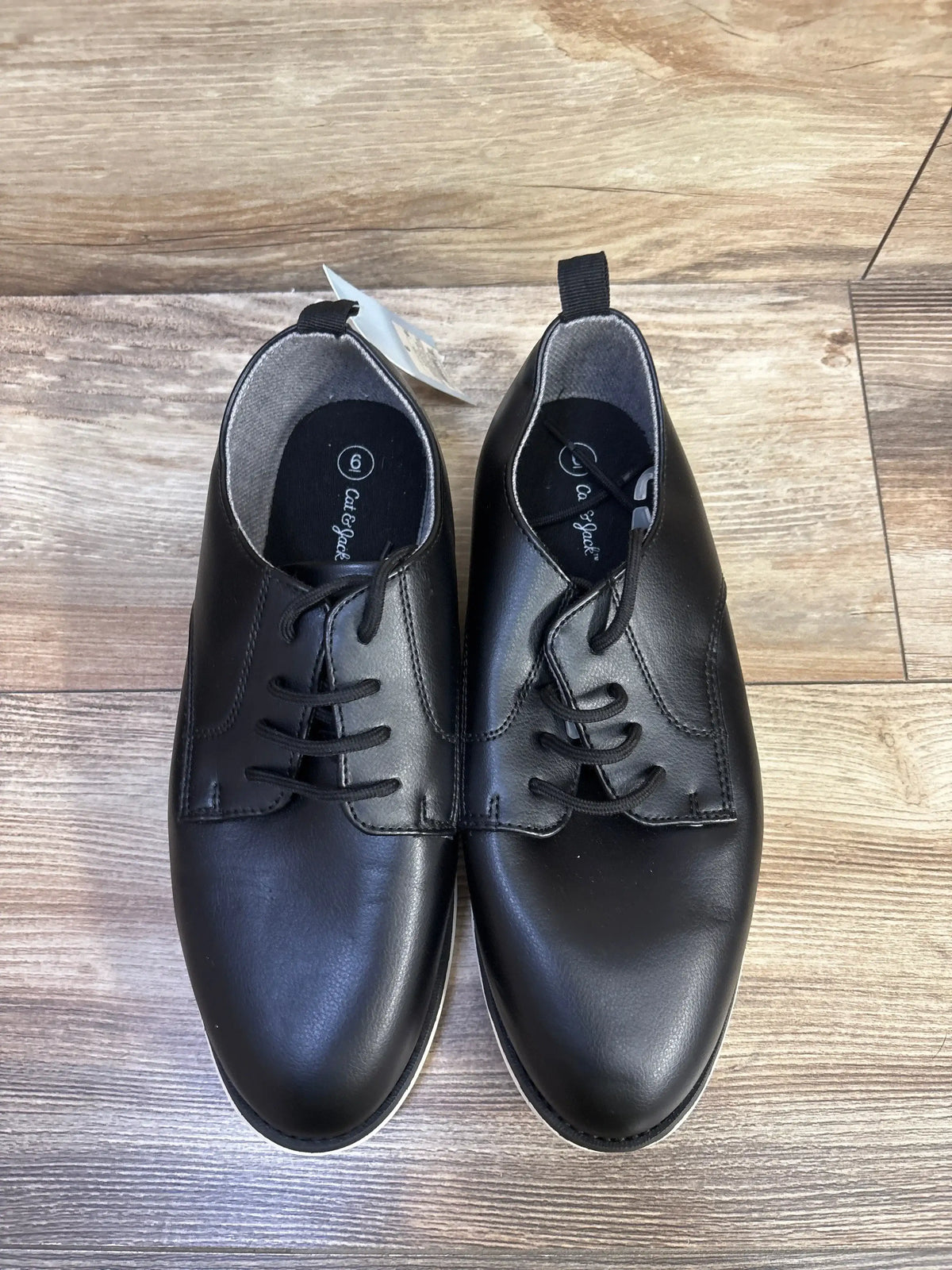 Top view of black Cat & Jack Alfi dress shoes in size 6Y showcasing lace closure with a wood floor background