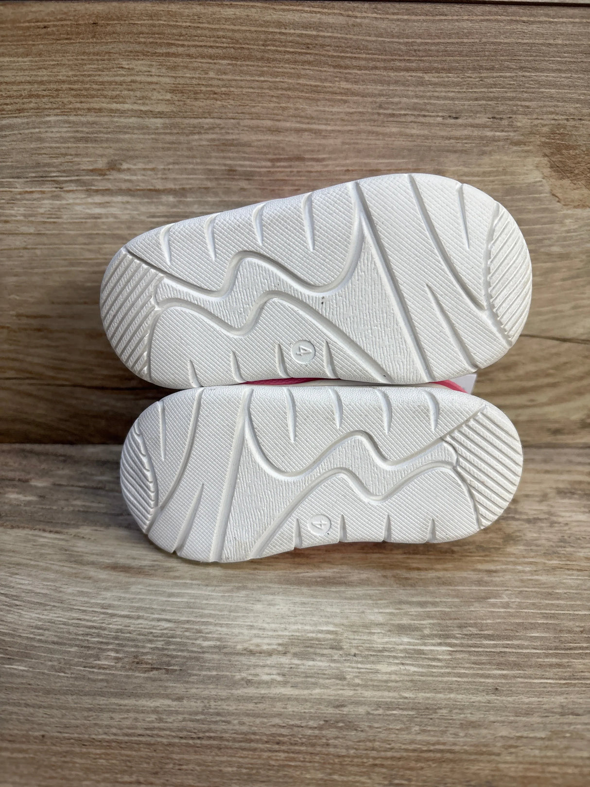 White rubber soles of toddler shoes with size 4, shown on wood floor