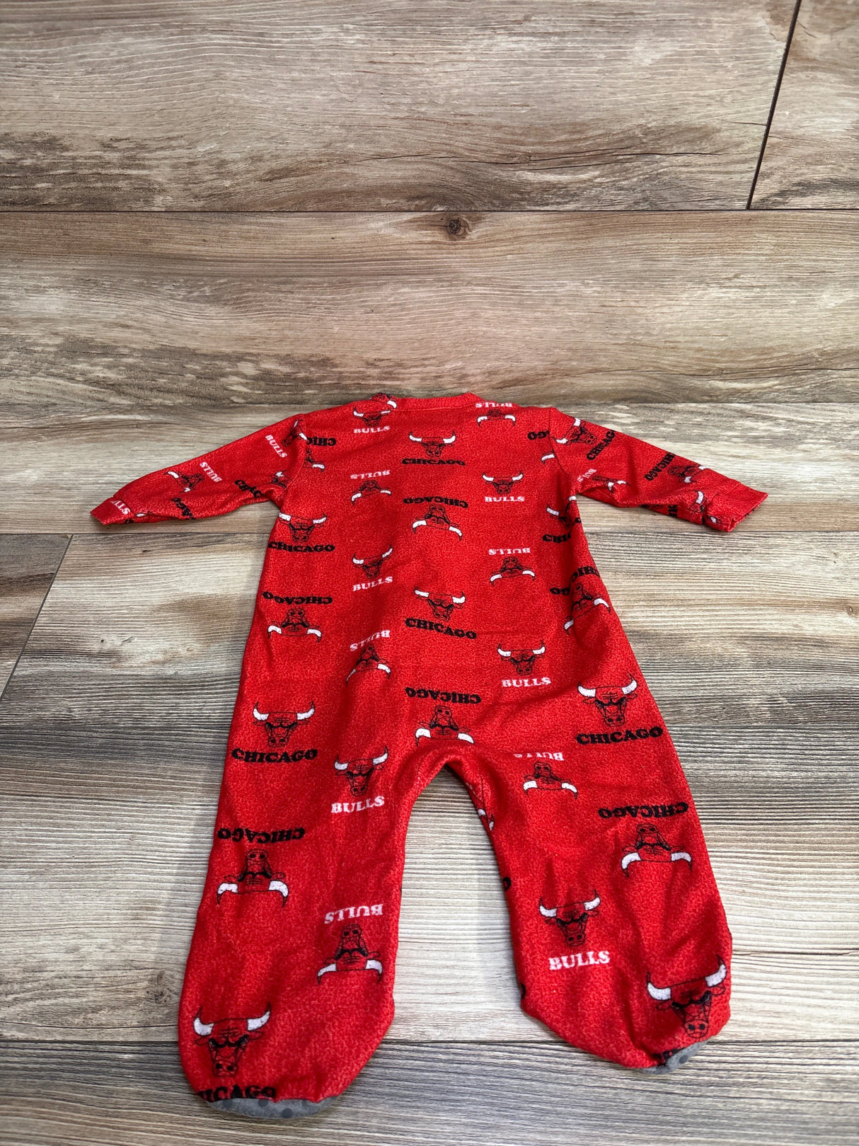 Red Chicago Bulls fleece baby sleeper with team logo and text, laid flat on wooden floor