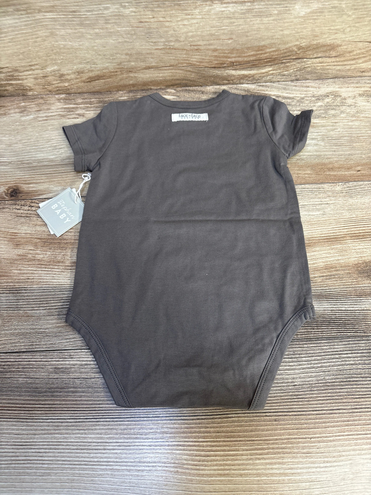 Back view of NEW Face To Face Lucky Charm Bodysuit in grey size 6-12m showcasing short sleeves with hangtag on wood plank floor