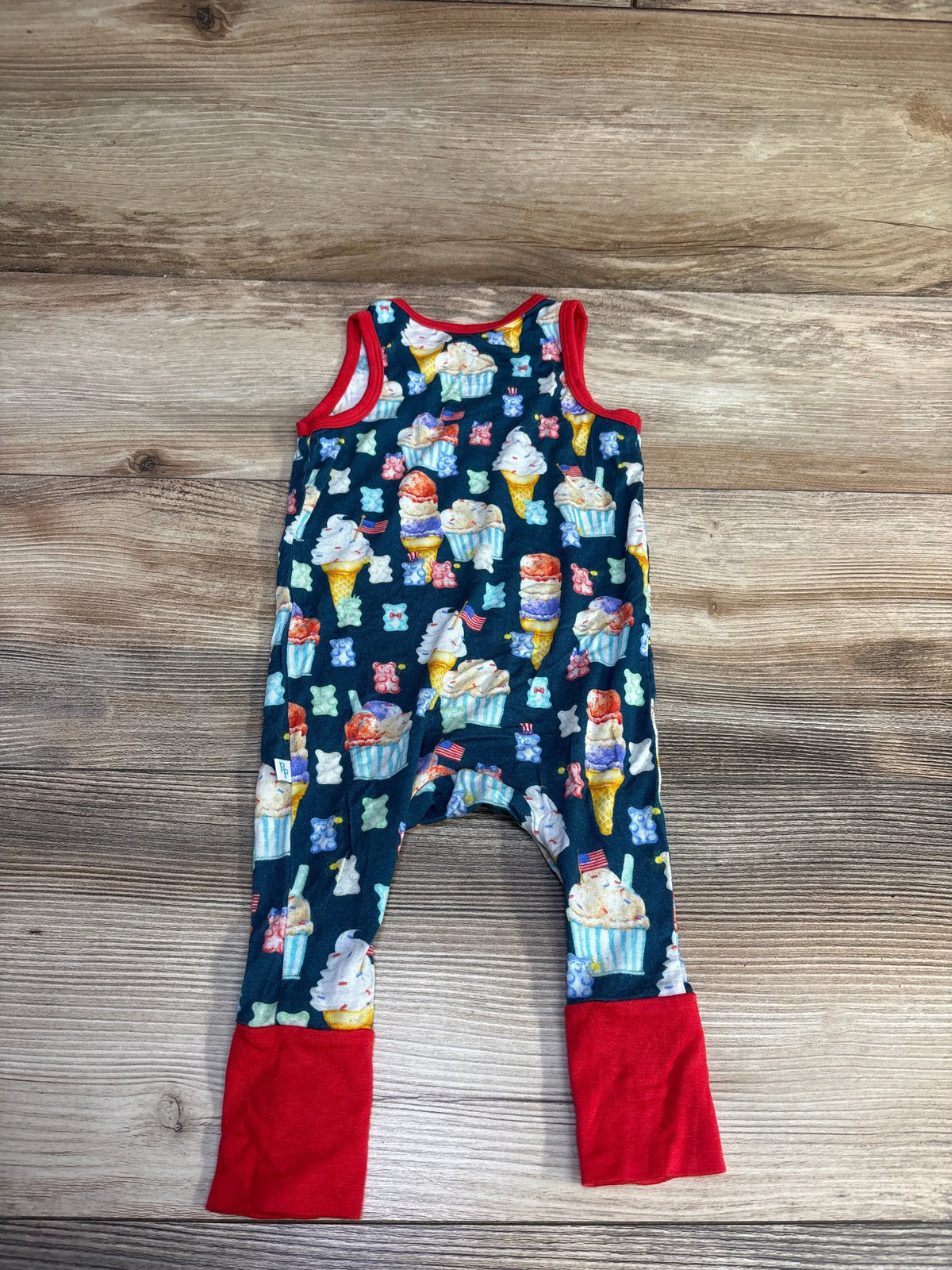 Front view of Posh P. bamboo sleeveless jumpsuit in blue, showcasing dessert print and red trim on a wood-grain background