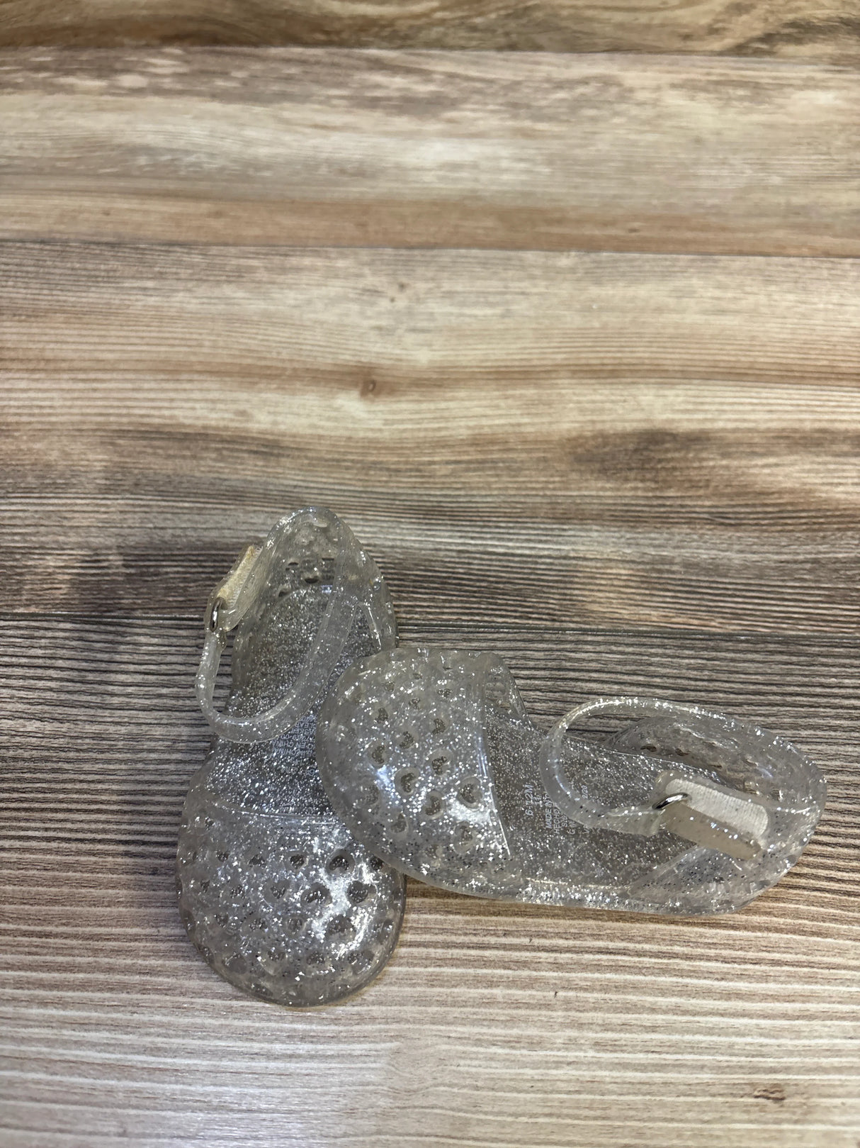 Top view of clear glitter toddler jelly sandals size 3C showing perforated toe and ankle strap on wood background