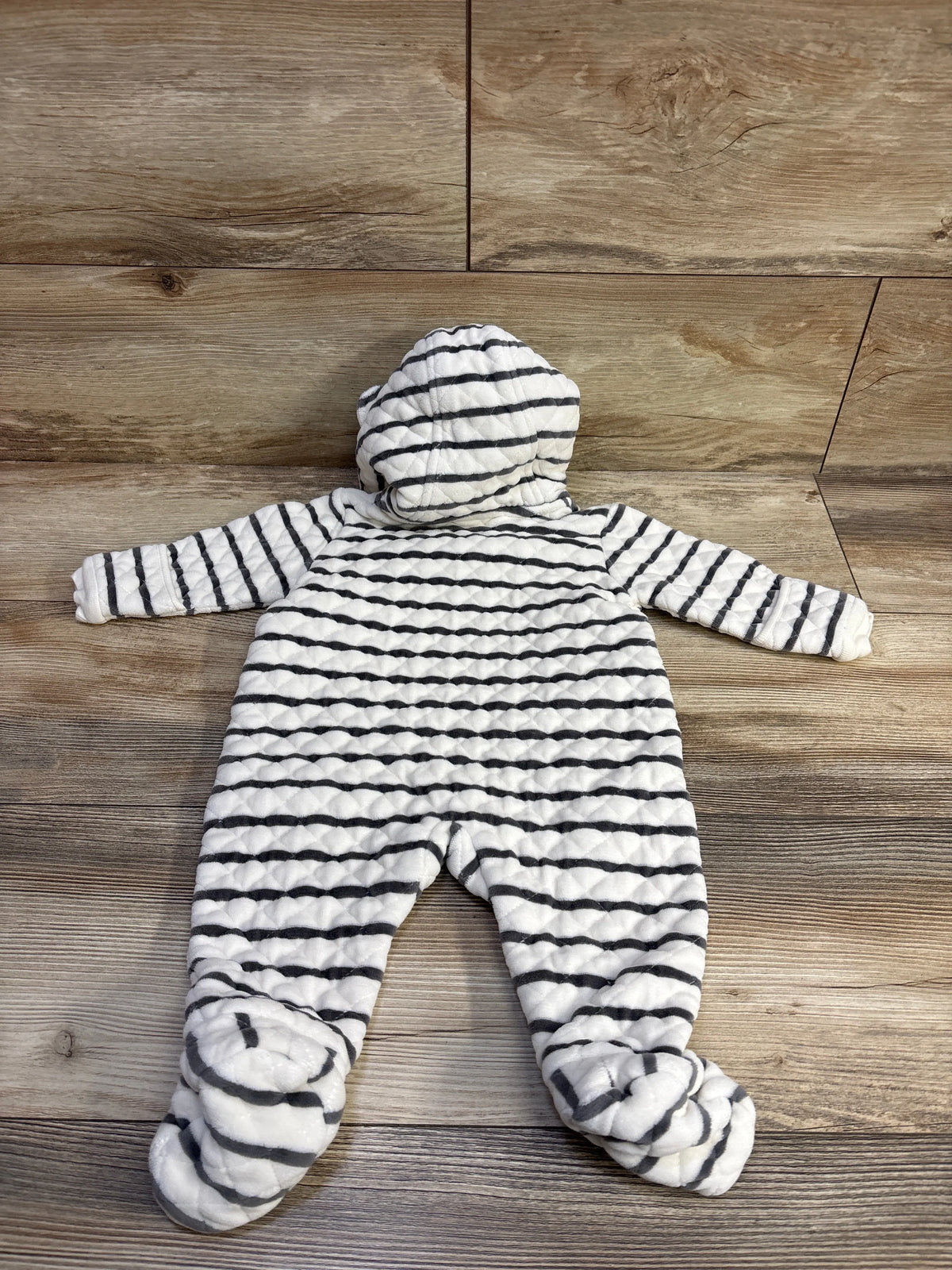 Flat lay of striped quilted baby bunting with hood and footed legs, black stripes on white, wood floor background
