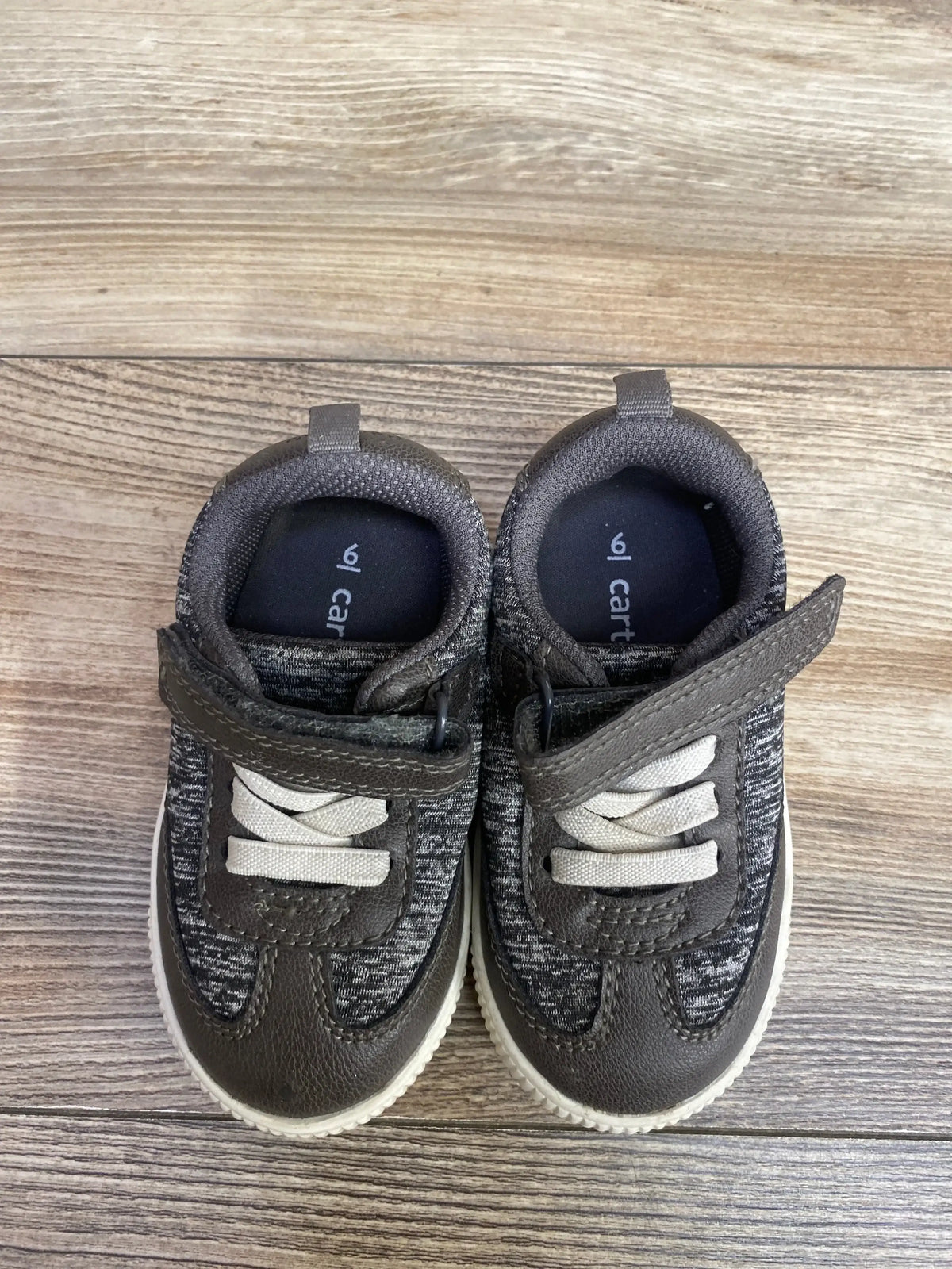 Pair of toddler gray and white sneakers with Velcro straps on wood floor