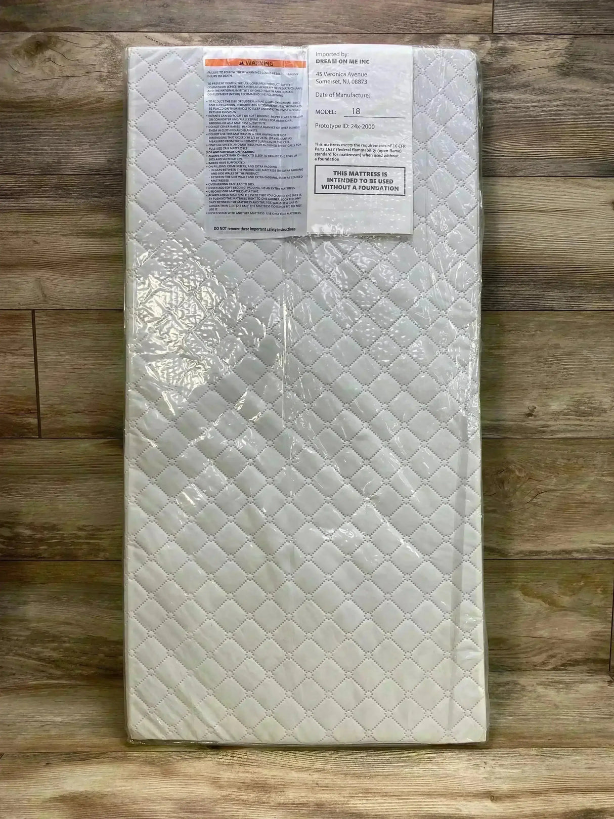 Top-down view of Dream On Me cradle mattress 36 x 18 x 2 inches showing quilted white cover in clear plastic packaging on wood floor