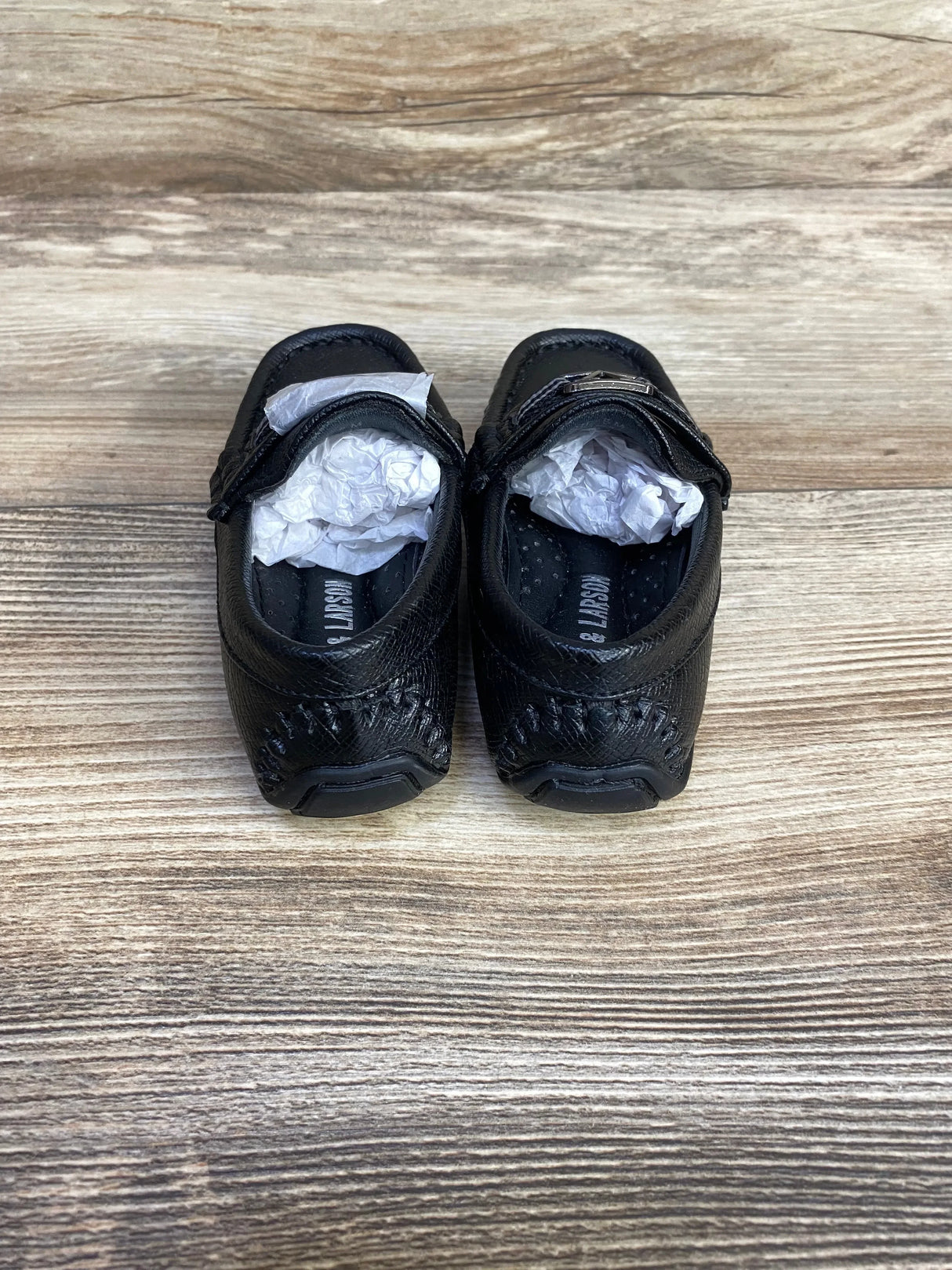 Top down view of black Curt and Larson loafers size 5C showing stitched heel detail and tissue stuffing on wood background