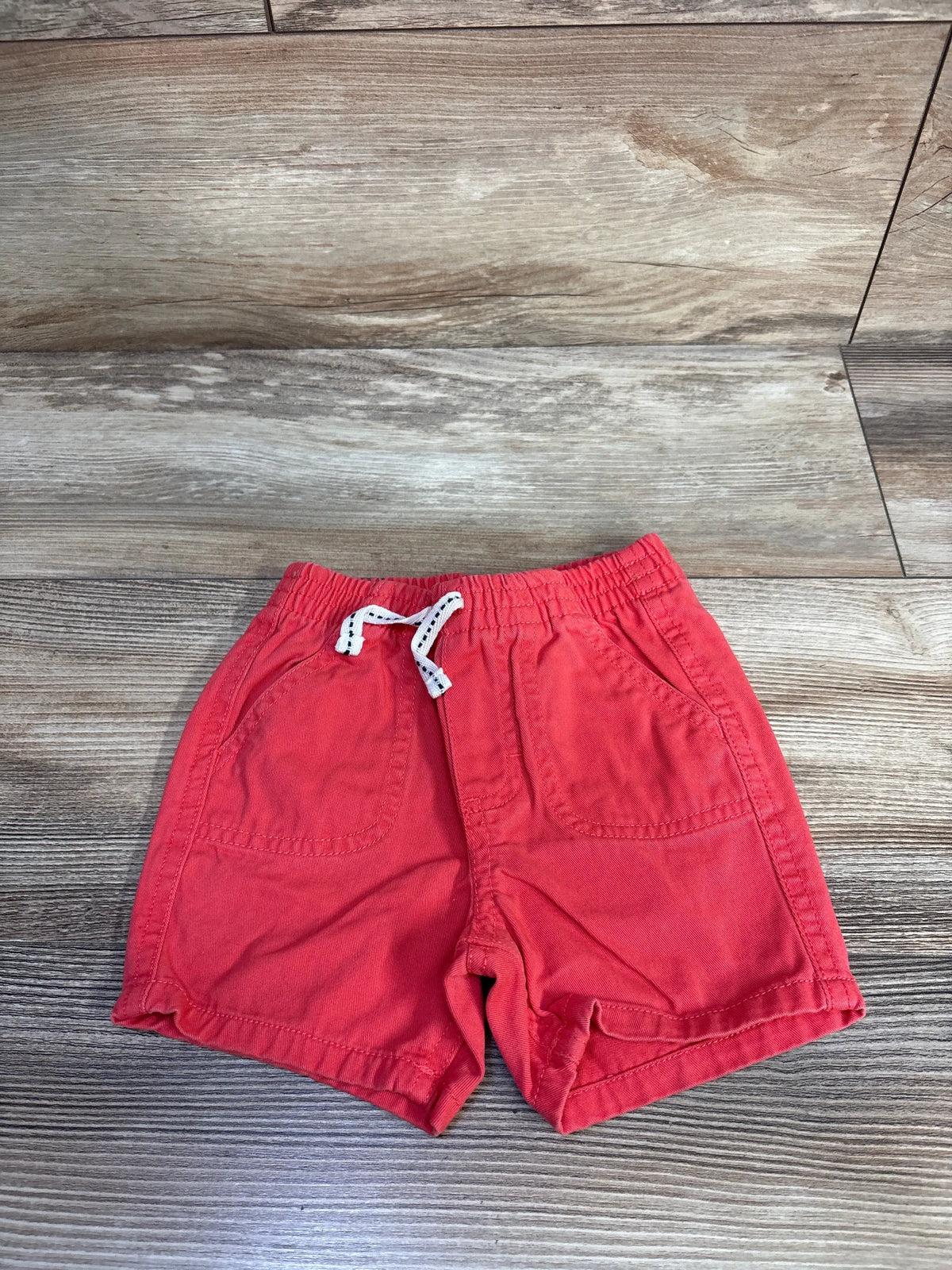Front view of Nautica red drawstring shorts showcasing elastic waistband, white drawstring, and front pockets on a wood-grain background