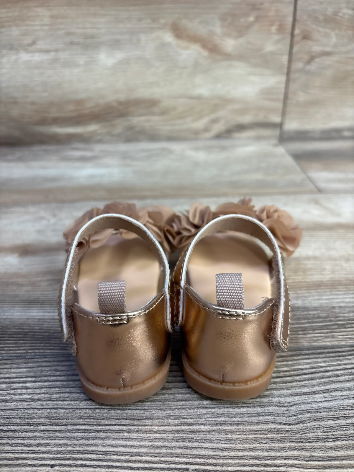 Rear view of H&M bronze flower sandals showcasing ankle straps on a wood-look background