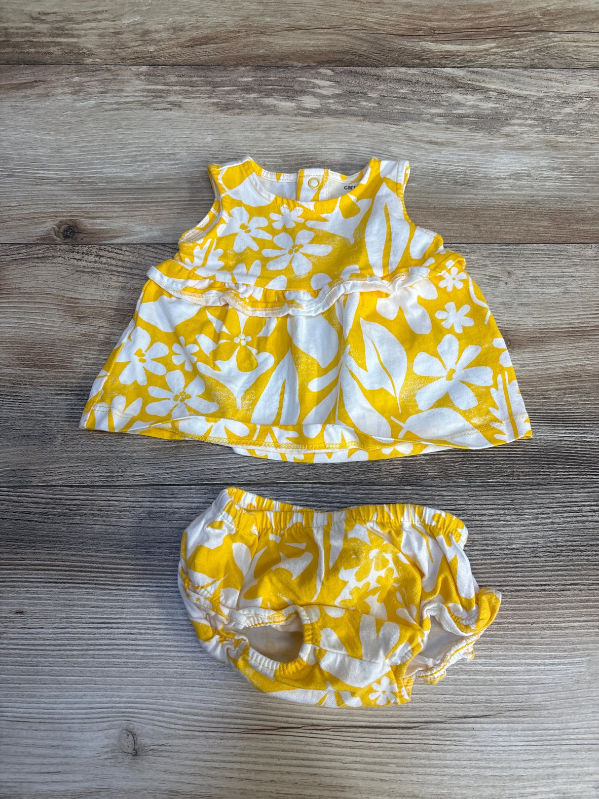 Yellow and white floral baby dress with matching bloomers, laid on wood floor