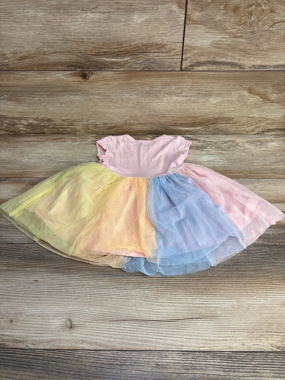 Flat lay of Carter's 18M rainbow tulle dress with pink bodice and pastel yellow, peach, blue, pink skirt on wood background