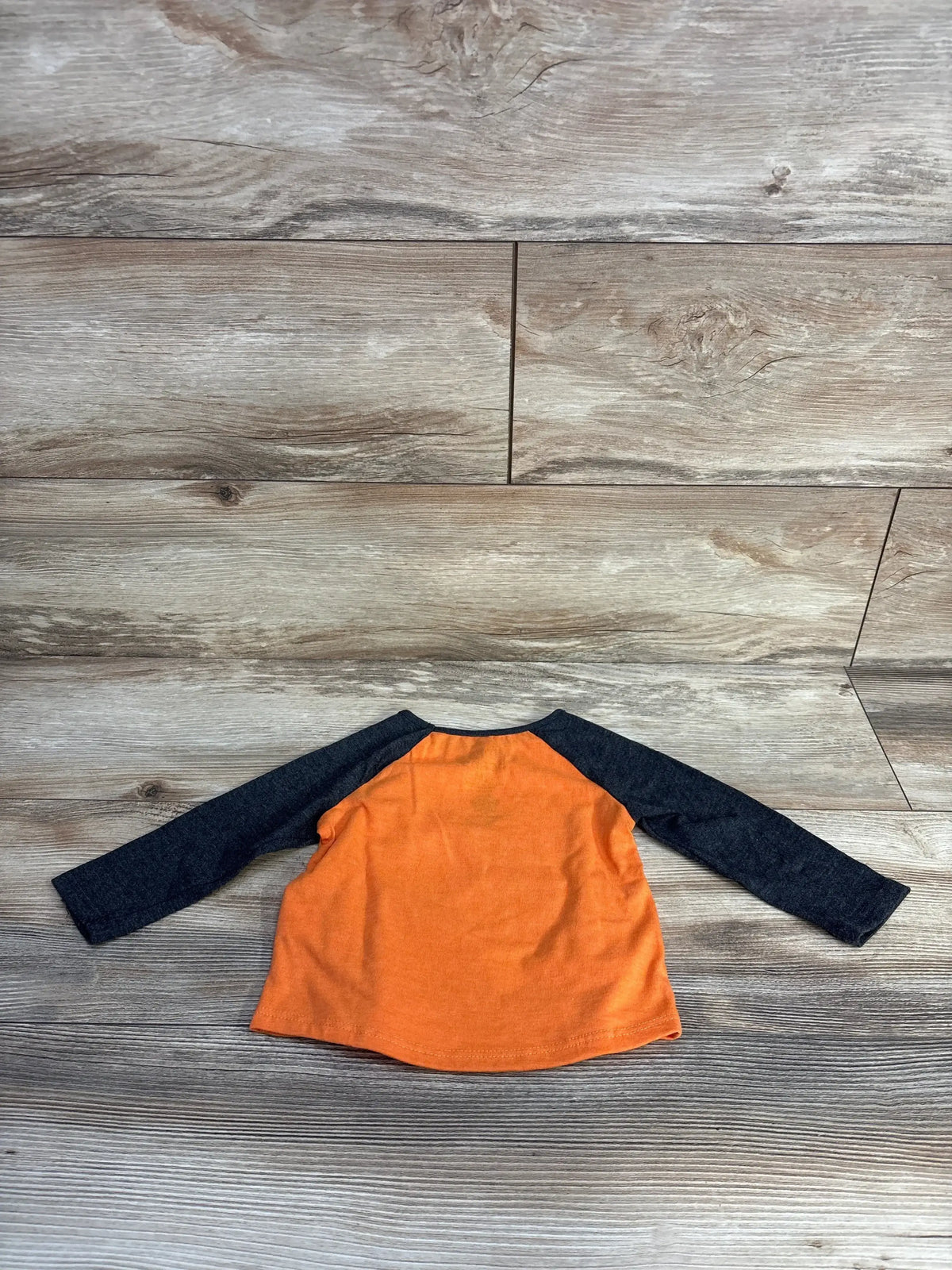 Back view of Jumping Beans Paw Patrol raglan shirt showing orange body and dark grey raglan sleeves on wood background