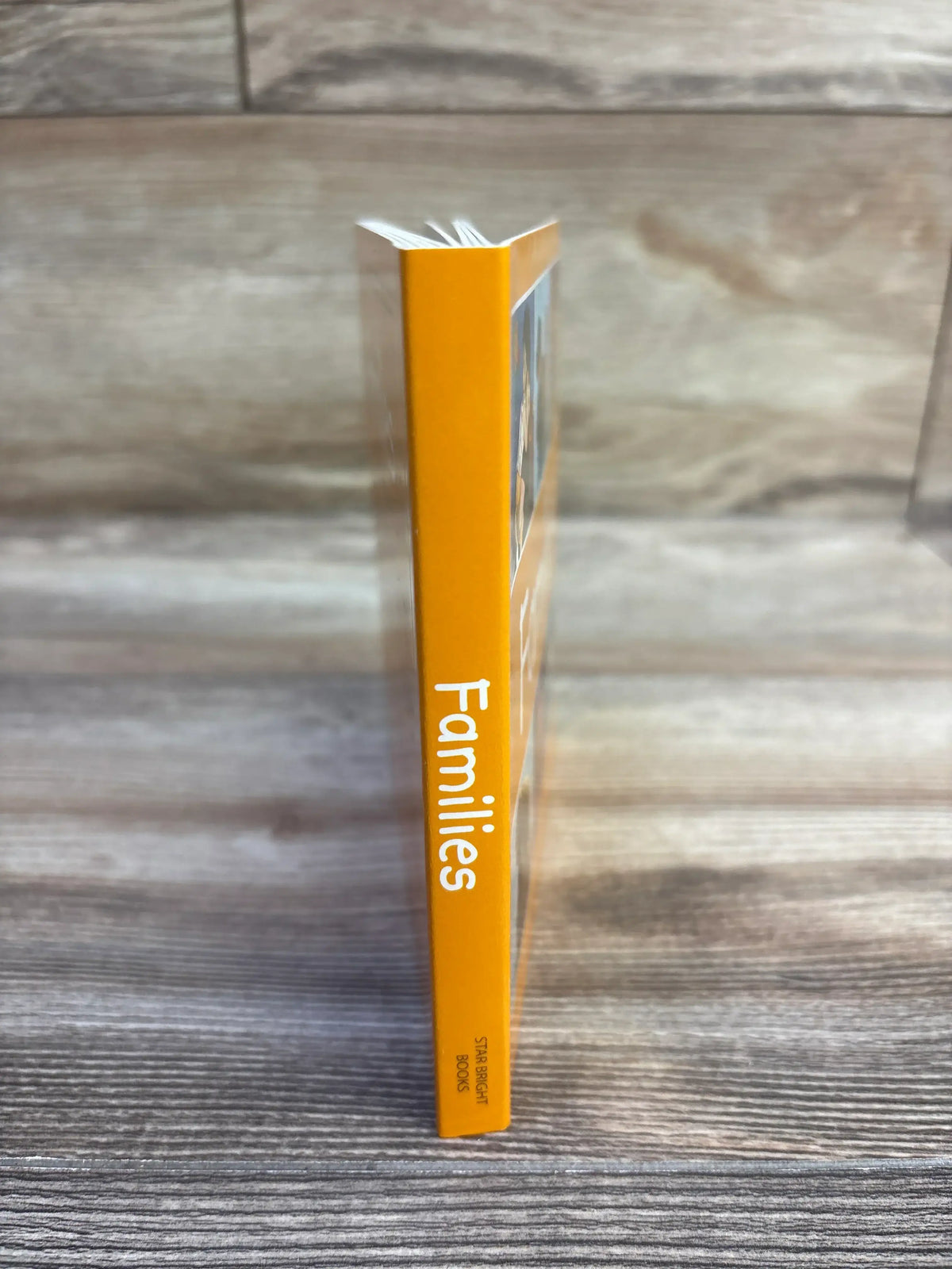 Side view of Families board book showing yellow spine with white “Families” title on wood-grain background